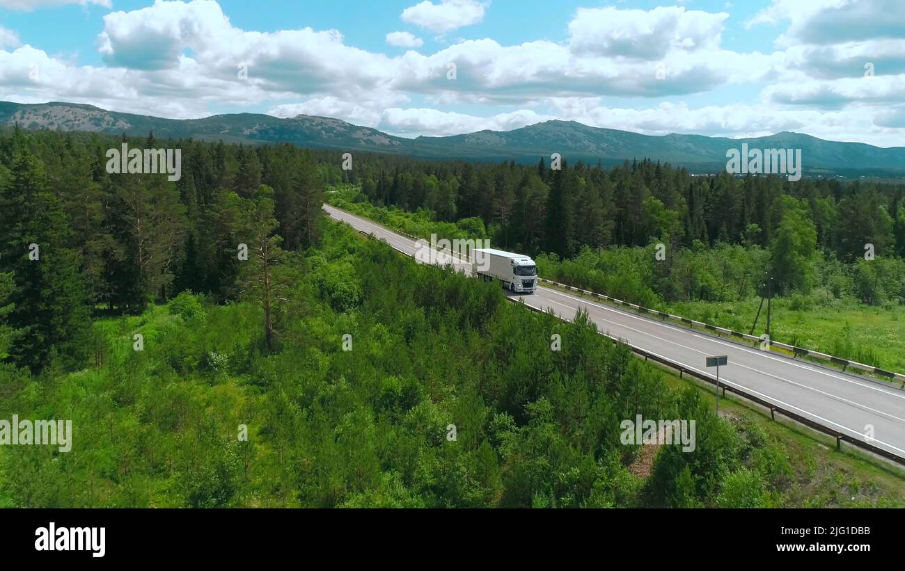 Draufsicht auf LKW, der am Sommertag entlang der Autobahn fährt. Szene. White Truck fährt auf einer Landstraße mit grünen Waldflächen. Trucker und fahrende tr Stockfoto