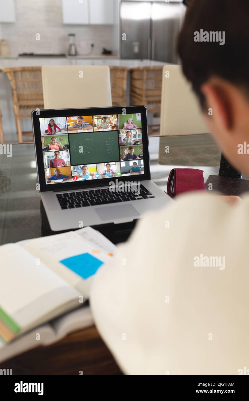 Asiatischer Junge mit Büchern auf dem Tisch, der zu Hause bei einem Videoanruf auf dem Laptop an einem Online-Vortrag teilnimmt Stockfoto