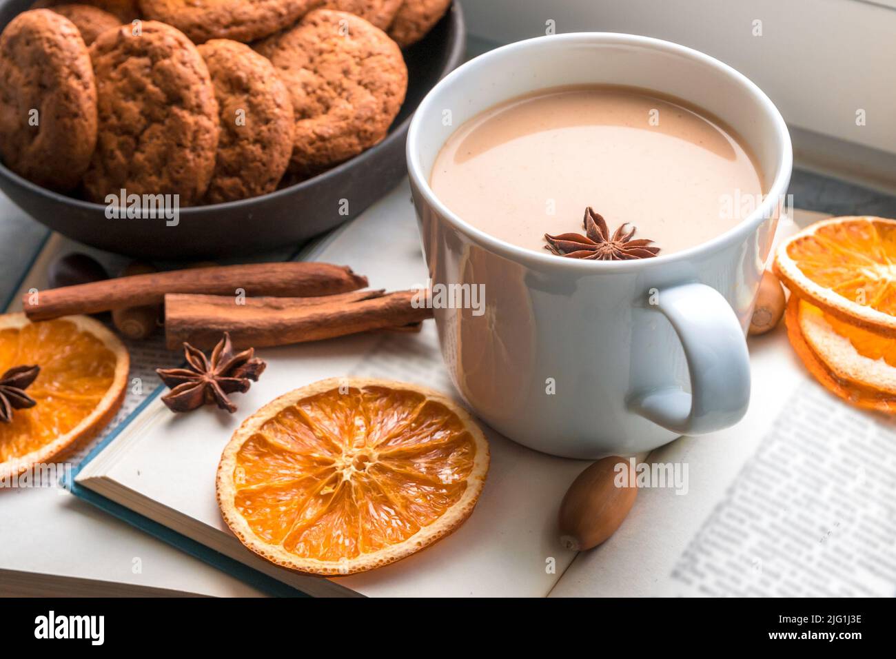 Eine große Tasse Kaffee und ein Buch am Fenster, mehrere Strickdecken und Scheiben getrockneter Orangen erinnern an den Herbst, eine gemütliche Zeit und einen Urlaub zu Hause. Stockfoto
