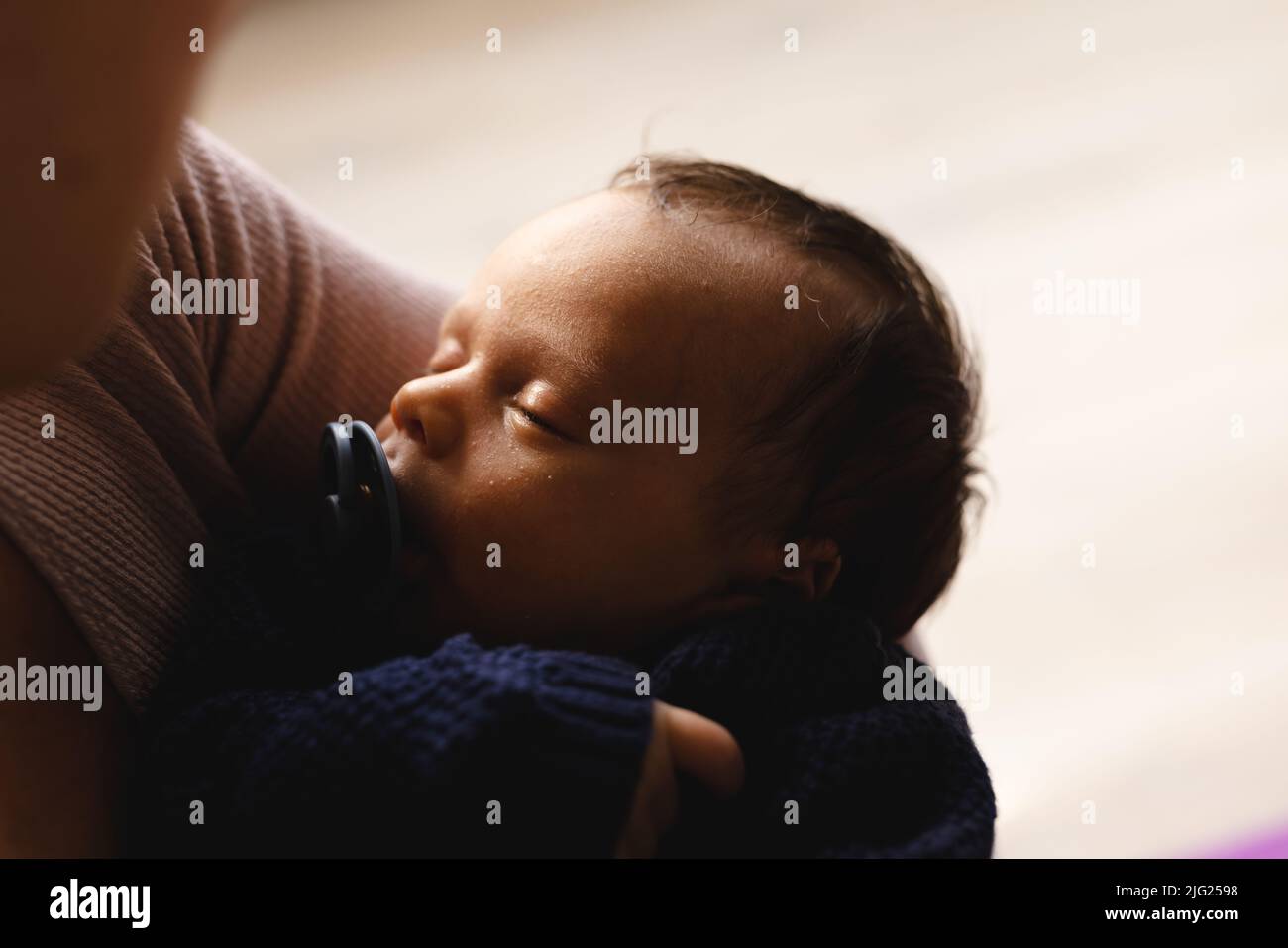 Nahaufnahme eines niedlichen schlafenden Neugeborenen mit Schnuller, der von der kaukasischen Mutter mittleren Erwachsenen zu Hause getragen wird Stockfoto