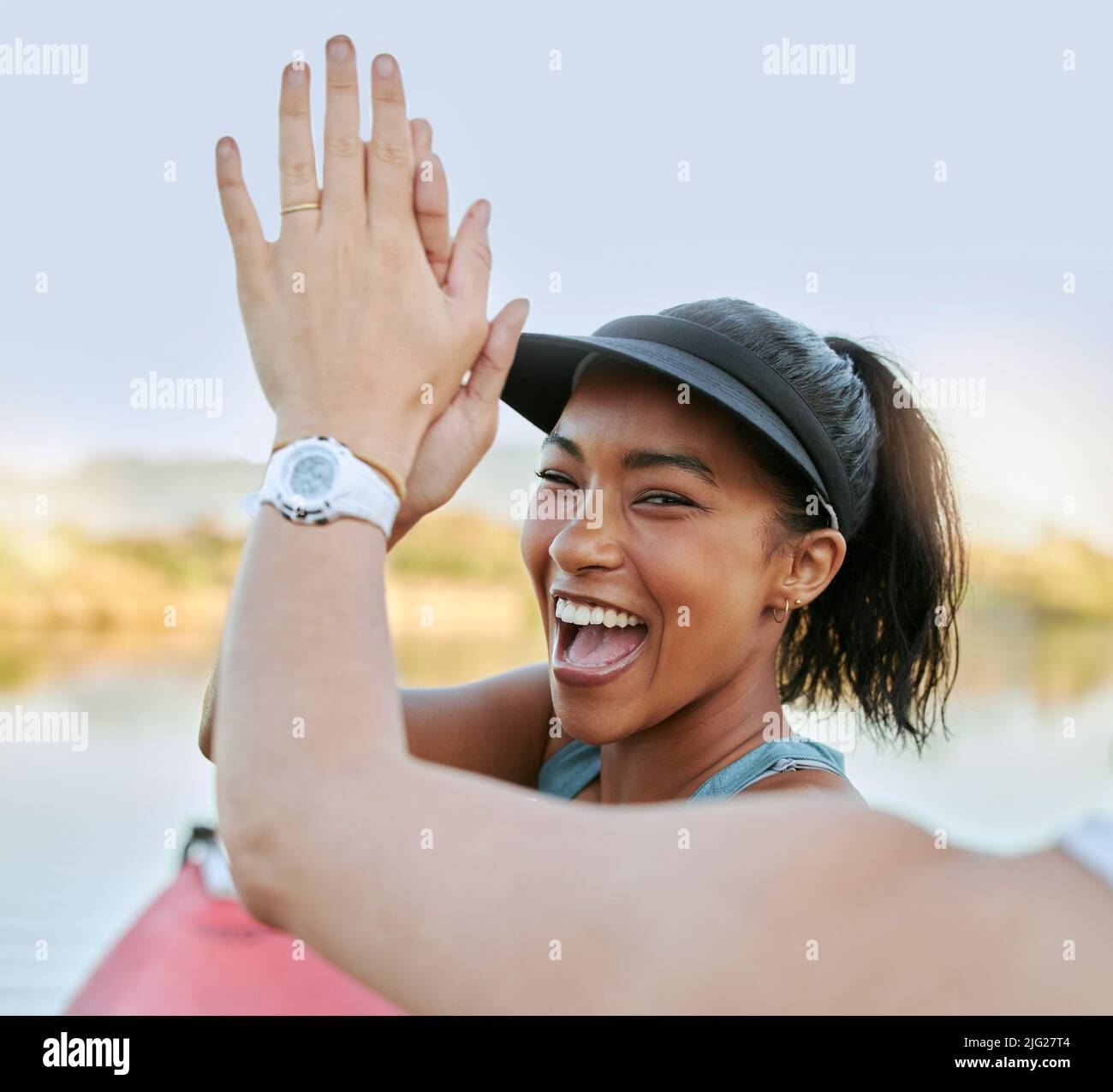 Zwei Freunde teilen sich High Five und feiern ihren Erfolg, während sie im Freien aktiv sind. Fröhliche Frau beim Kajakfahren und Motivieren ihres Partners während Stockfoto