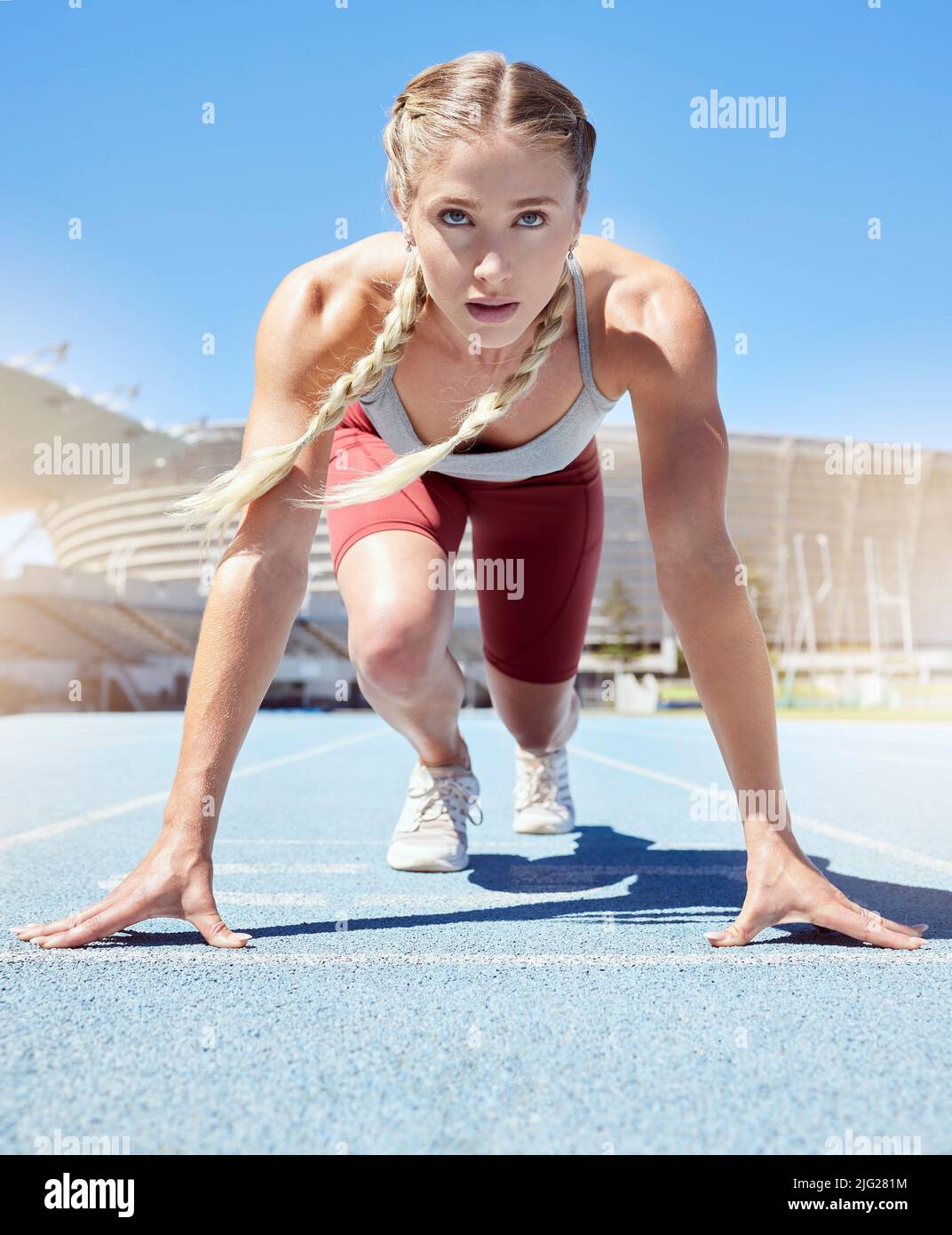 Seriöse weibliche Athletin an der Startlinie bei einem Bahnrennen im Stadion. Fit Sportlerin geistig und körperlich bereit zu starten Stockfoto