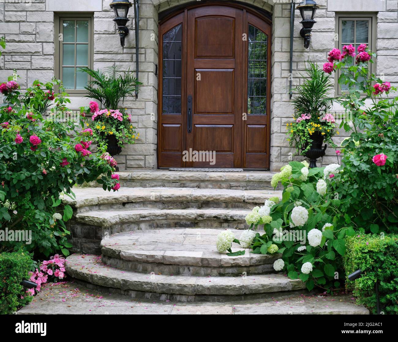 Haupteingang mit eleganter hölzerner Haustür, umgeben von wunderschönen Blumen Stockfoto