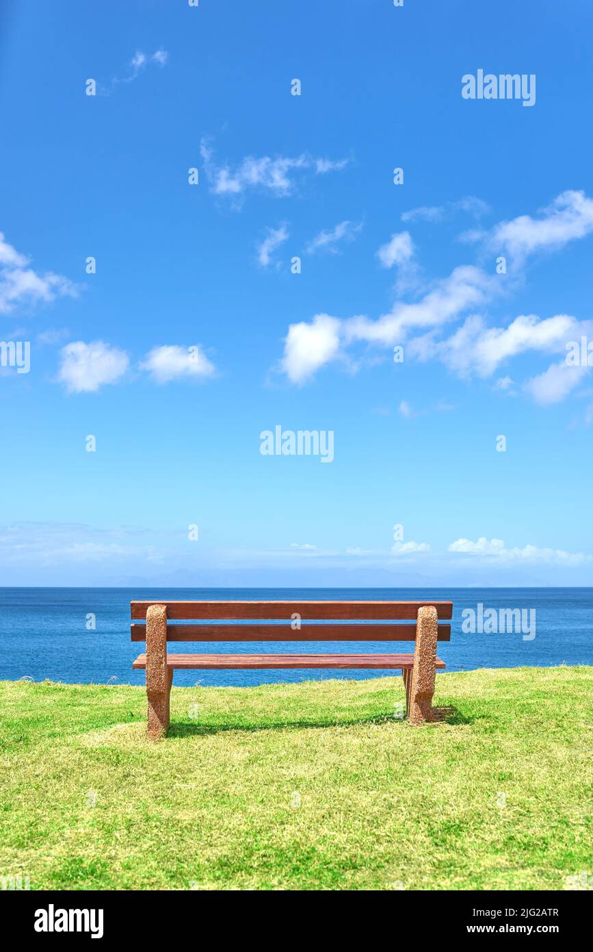 Schöner Blick auf den Strand von einer Bank mit Kopierplatz an einem Sommertag mit einem blauen Himmel Hintergrund. Friedliche und ruhige Meereslandschaft mit einem Sitz an der Küste Stockfoto