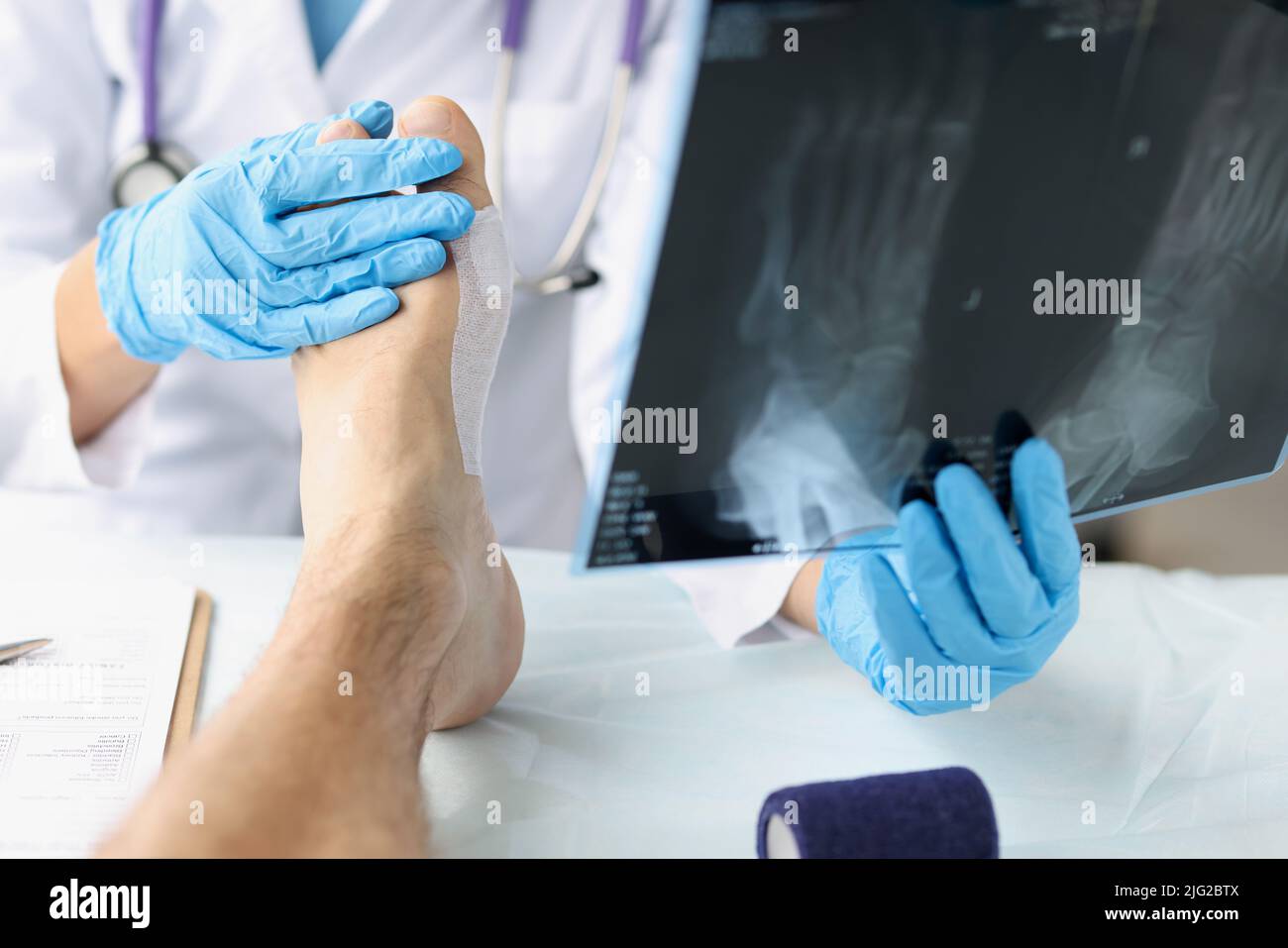 Traumatologe, der die Röntgenaufnahme des Fußes betrachtet und den Patienten untersucht Stockfoto