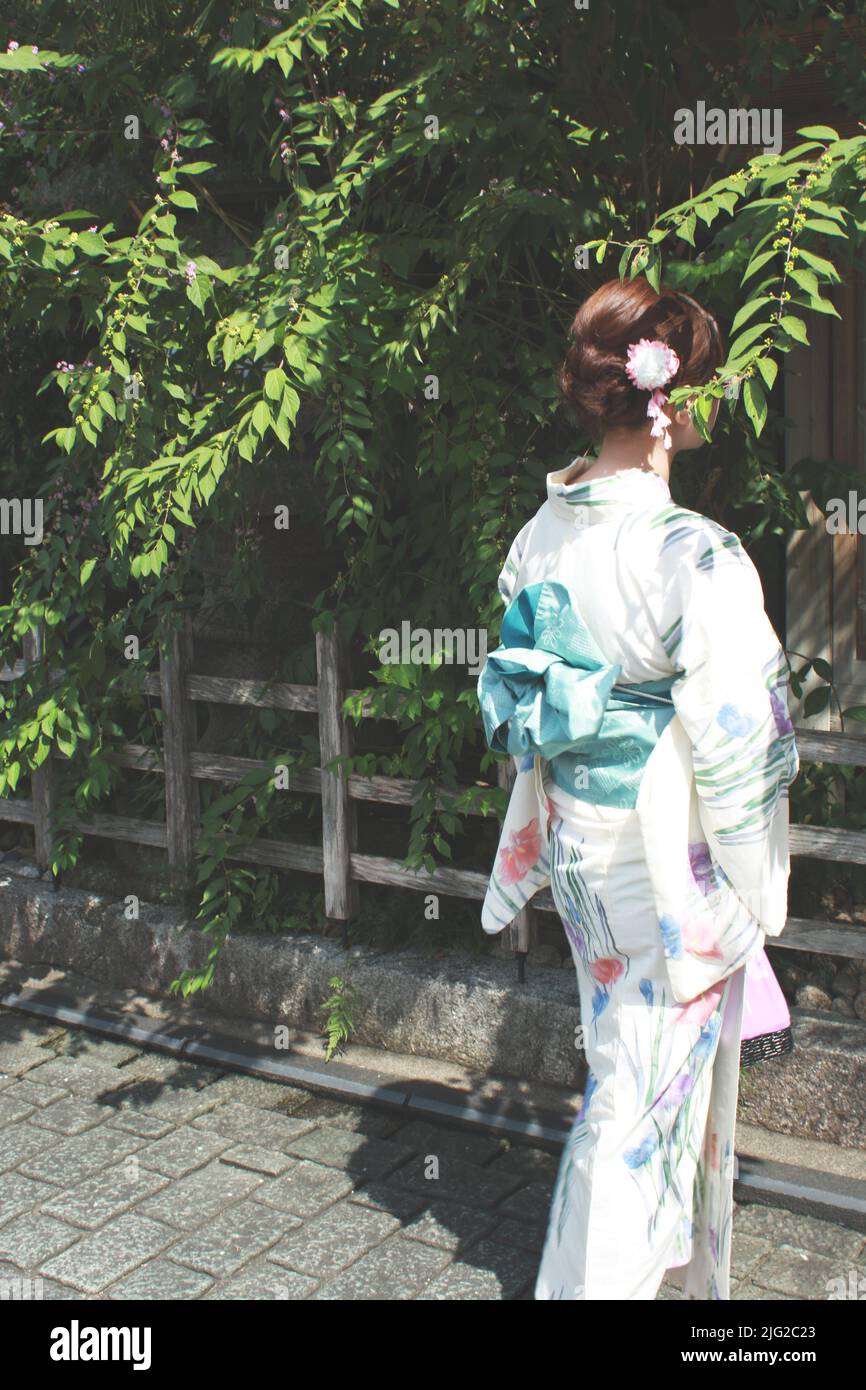 Die Rückseite einer japanischen Frau, die eine traditionelle Yukata unter den Bäumen trägt. Stockfoto