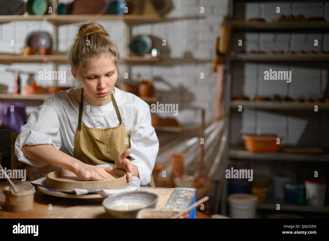 Ein Keramiker macht einen Teller. Frau in einer Schürze arbeitet in einer Töpferwerkstatt. Stockfoto