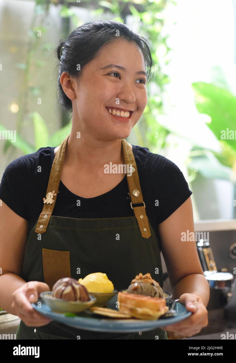 Vietnamesisches Mädchen, das in einem Café hausgemachtes Eis mit Waffeln serviert. Stockfoto