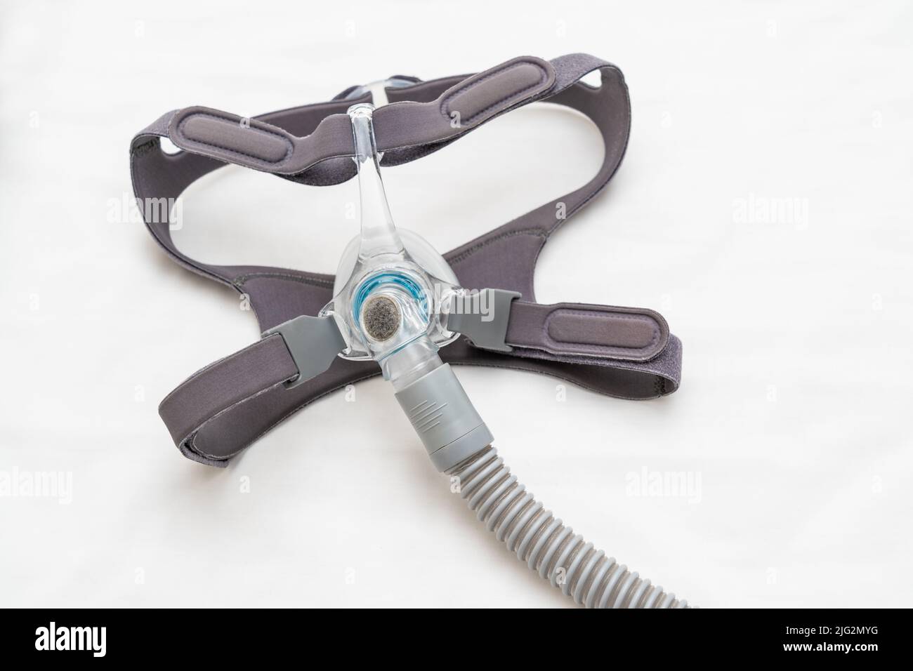 CPAP-Maske und Kopfbedeckungen werden mit einem CPAP-Schlauch auf weißem Bettlaken verbunden Stockfoto