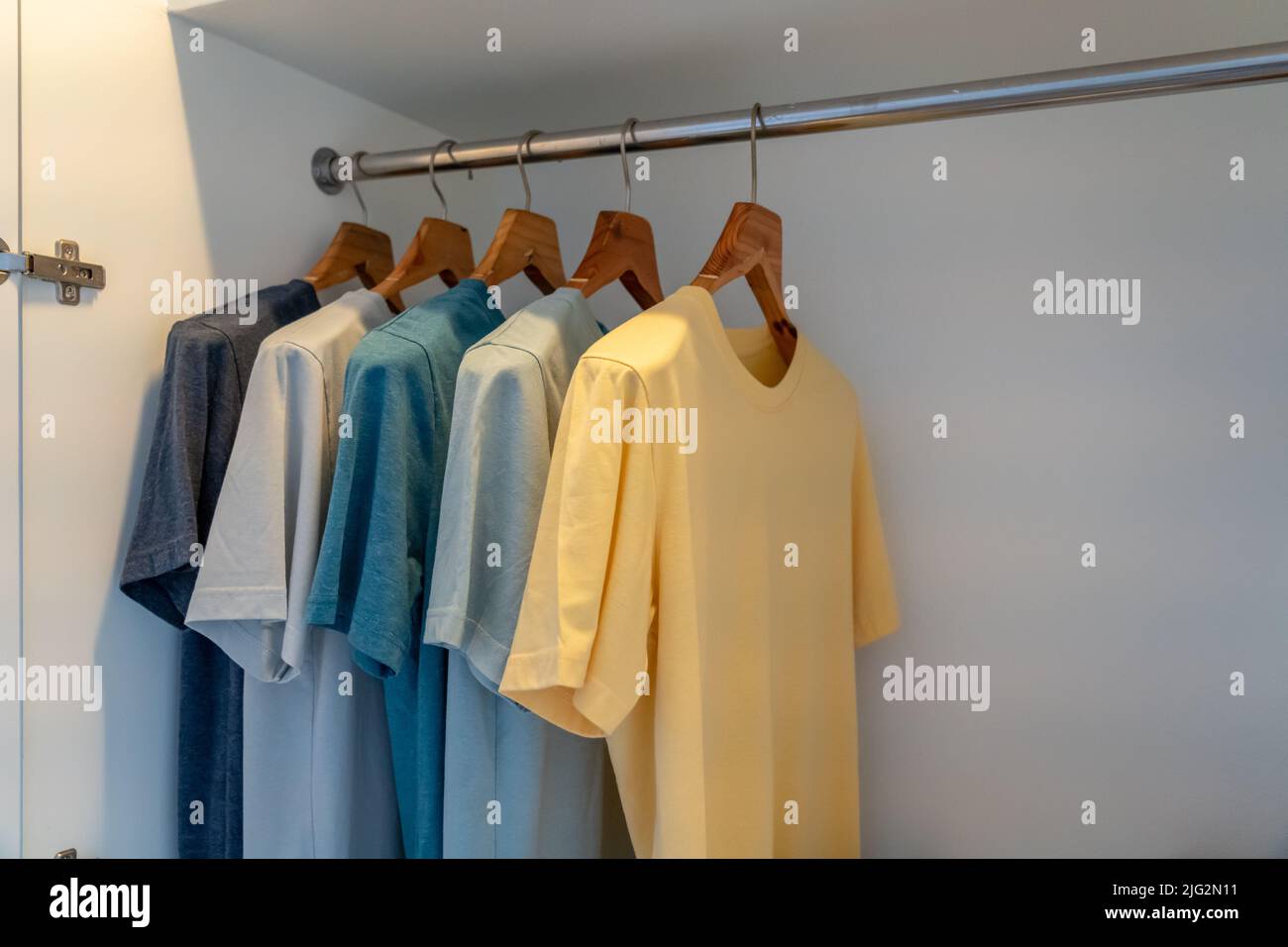 In einem weißen Schrank hängendes T-Shirt aus Baumwolle in gleichem Stil in einfarbiger Farbe Stockfoto