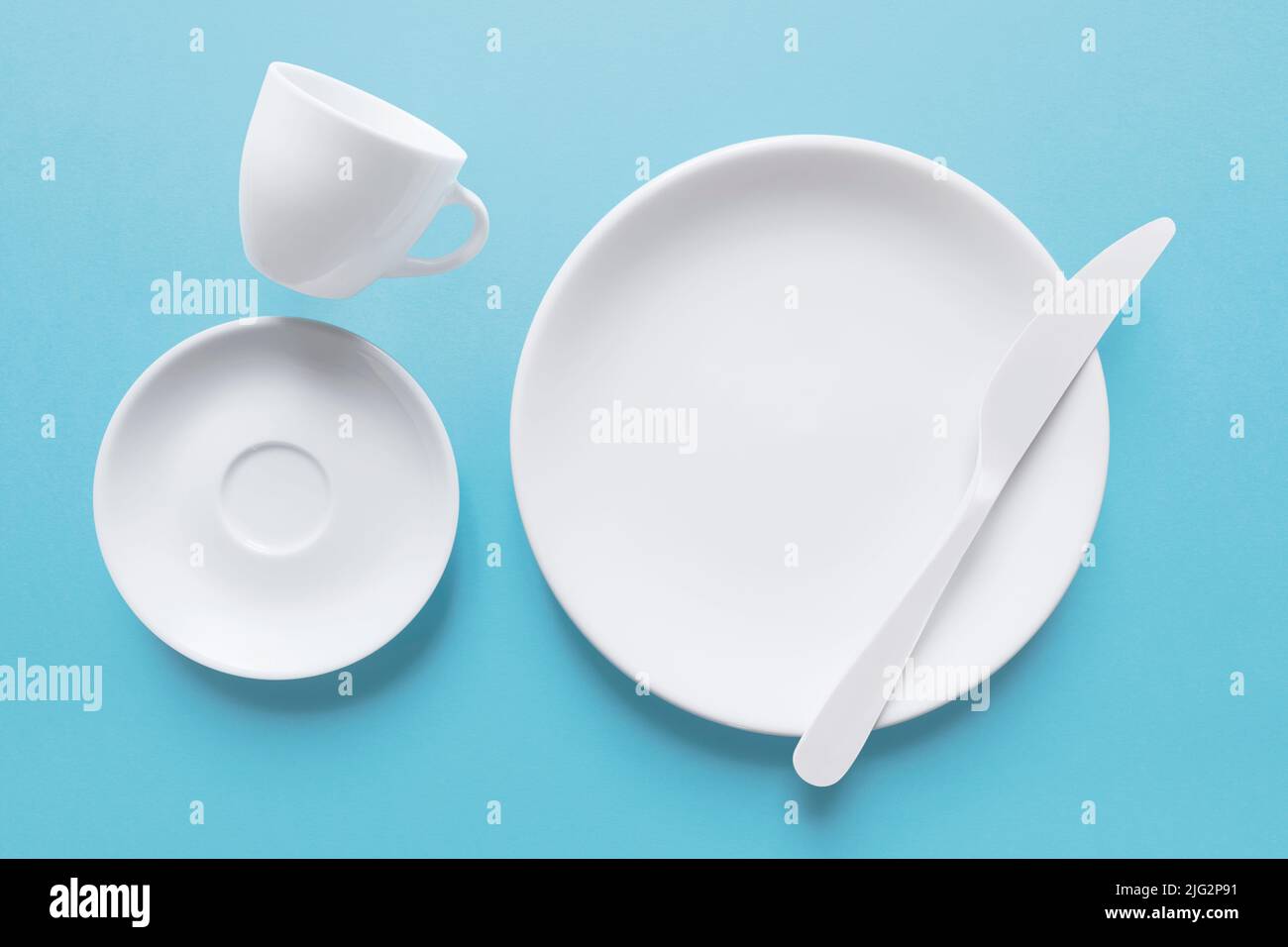 Weiße Kaffeetasse und Schale mit Messer, isoliert auf hellblau Stockfoto