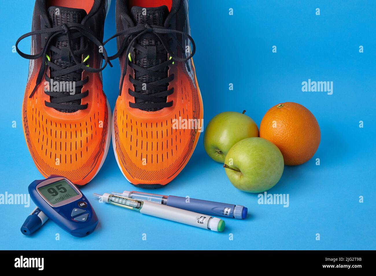 Orangefarbene Sneakers, Früchte, Maßband, Glucometer und Insulin-Spritzenstifte auf blauem Hintergrund. Bewegung, Ernährung, Injektion und Diabetes managen Stockfoto