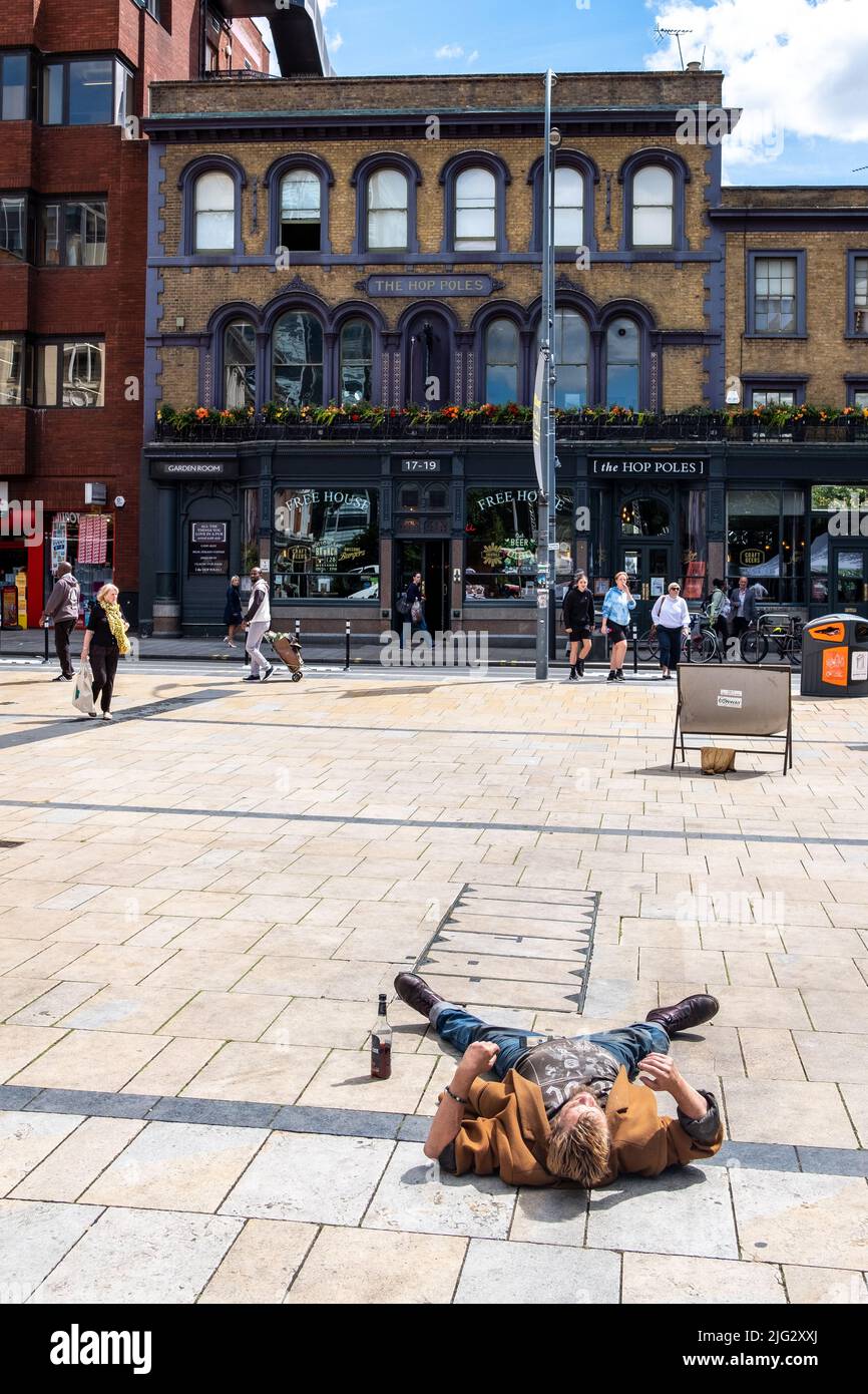 London - 2022. Juni: Ein betrunkener Mann auf dem Boden mit einer Kneipe im Hintergrund in Hammersmith, West-London Stockfoto