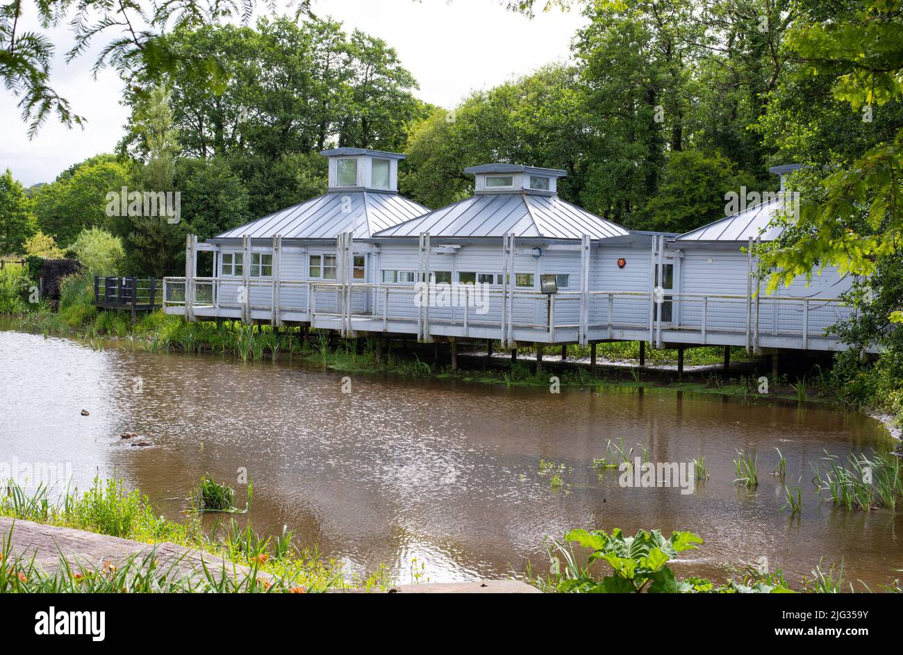 Das im Juli 2022 im National Botanic Garden Wales aufgenommene Foto zeigt das Wasserpflanzenhaus auf Stelzen auf der anderen Seite des Teiches. Stockfoto