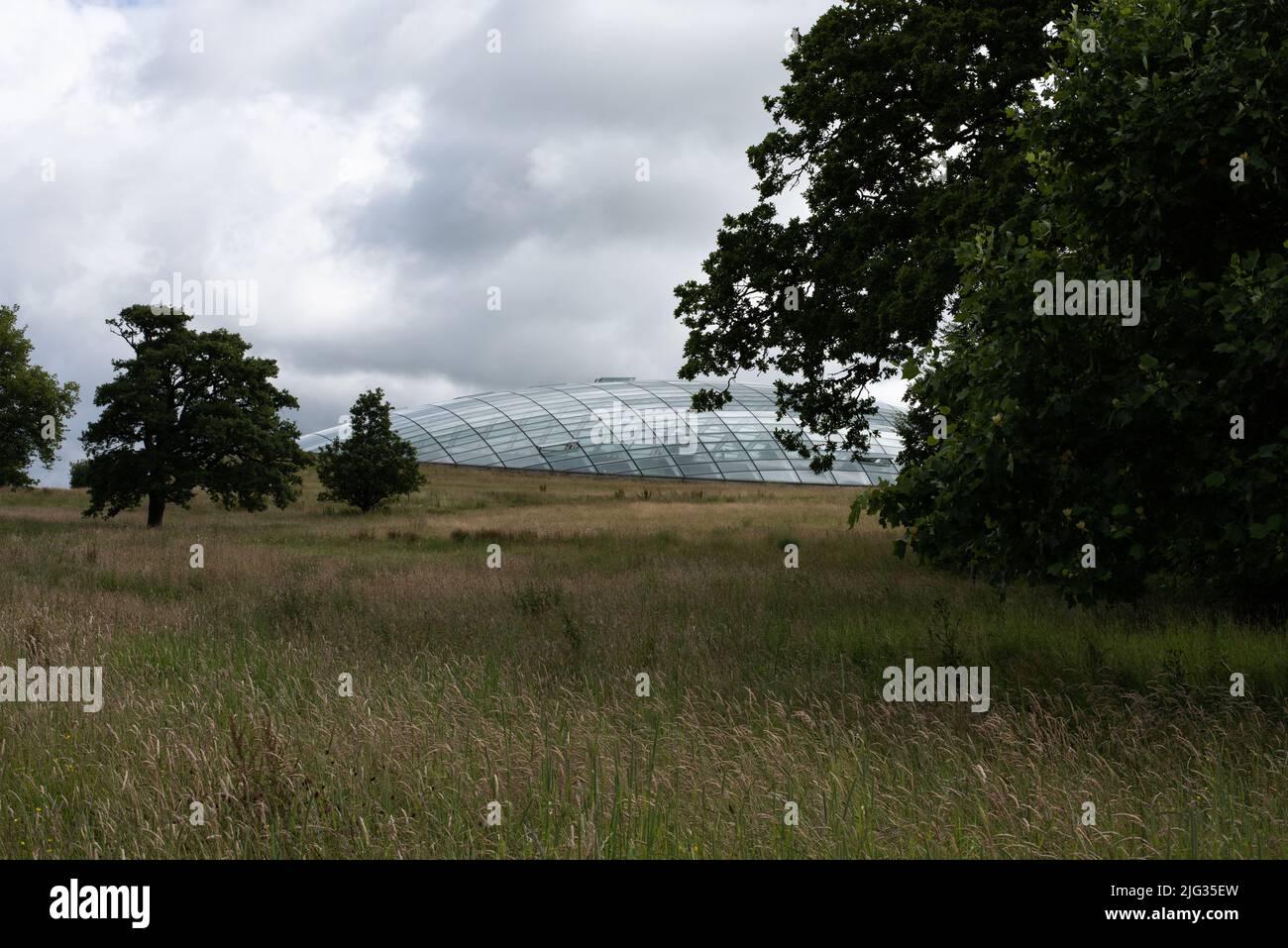Das Foto wurde im Juli 2022 im National Botanic Garden Wales aufgenommen und zeigt einen launischen Himmel über dem größten, einspangigen Gewächshaus der Welt. Stockfoto