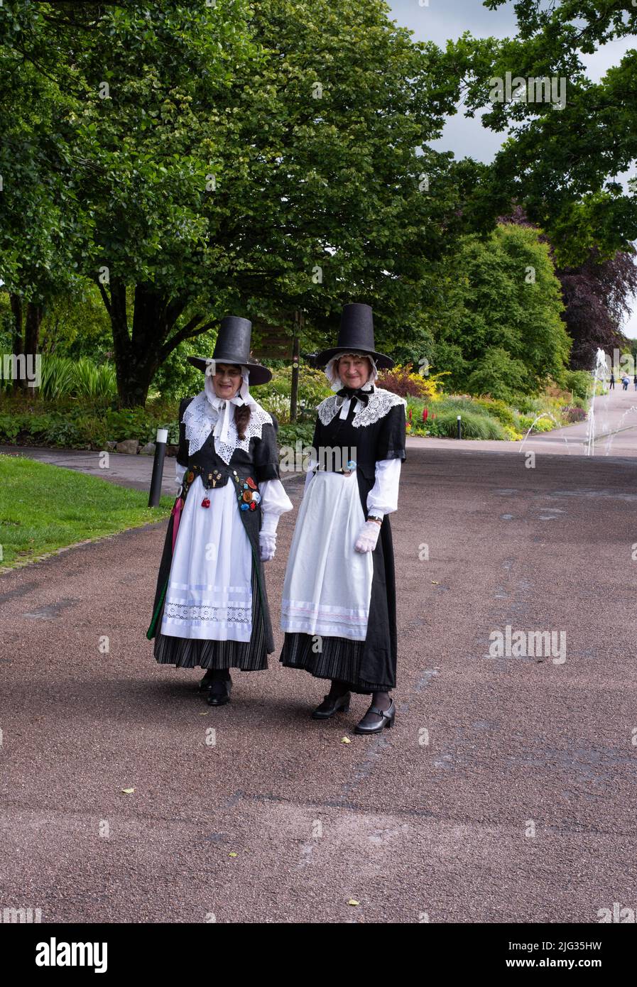 Das Foto wurde im Juli 2022 im National Botanic Garden Wales aufgenommen und zeigt zwei der vielen Volkstänzer, die traditionelle Ofenpfeifenhüte und Spitzenhalsbänder tragen. Stockfoto