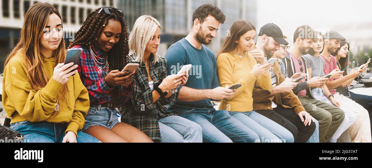 Gen z verschiedene Menschen mit Handys sitzen auf einer Bank im Freien, Panorama. Lifestyle-Konzept mit multirassischen Männern und Frauen, die Smartphones nutzen. Gadge Stockfoto
