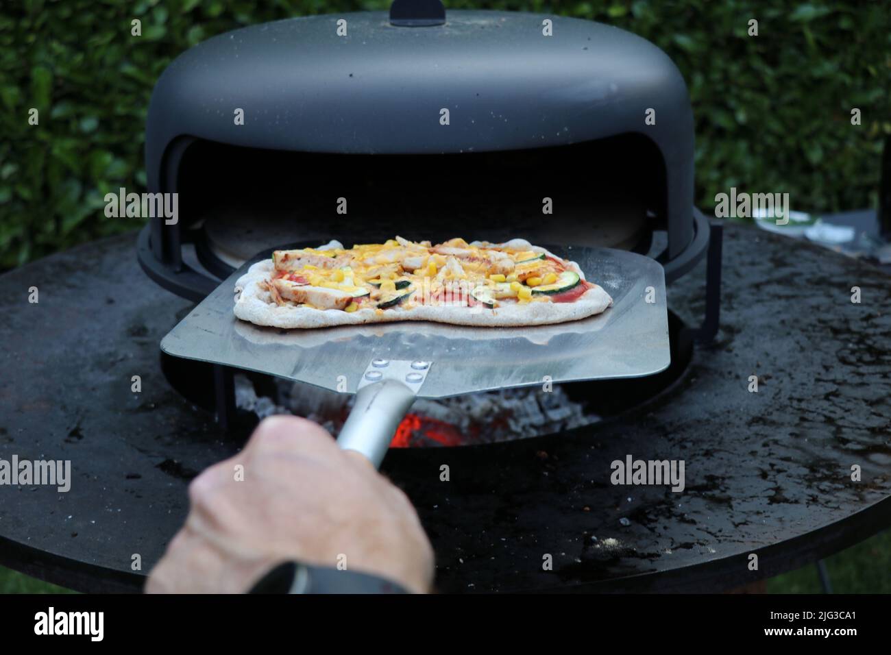 Eine hausgemachte, rustikale Pizza, die aus einem Holzofen im Freien genommen wird Stockfoto