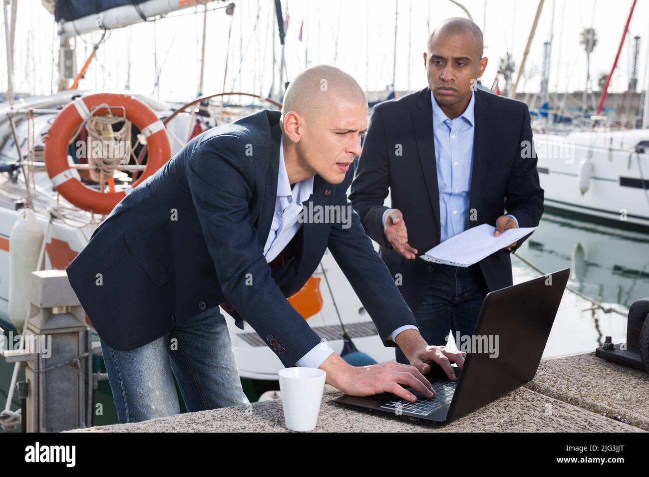 Männer in Anzügen, die die Dokumentation auf einem Laptop im Seehafen verifizieren Stockfoto