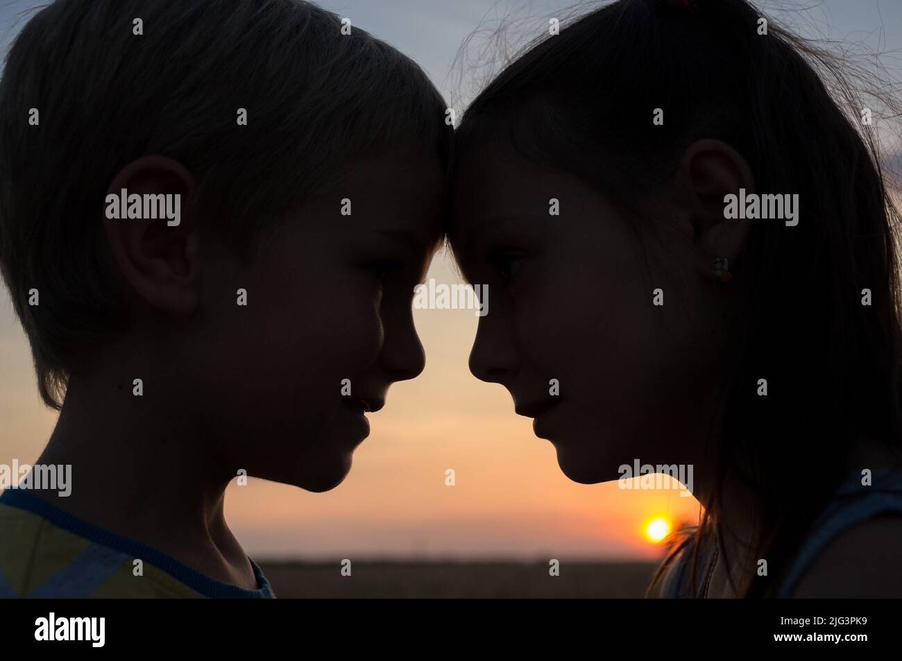 Nahaufnahme der Köpfe eines Jungen und eines Mädchens, die ihre Stirn vor dem Hintergrund der untergehenden Sonne gegeneinander drücken. Zartes Gefühl Stockfoto