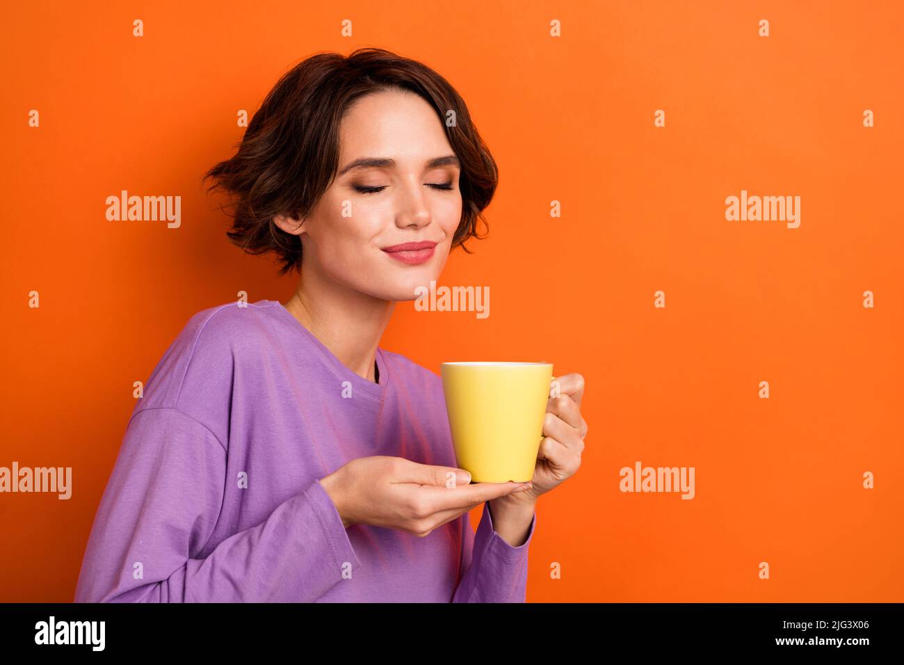 Portrait of Charming entzückende Dame geschlossenen Augen riechen Kaffee isoliert auf orangefarbenem Hintergrund Stockfoto