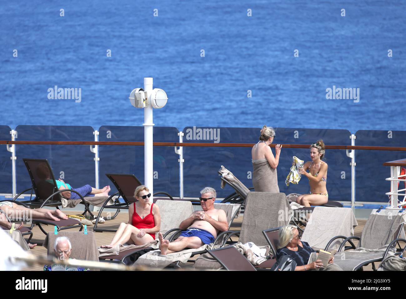 Massen von reifen Passagieren entspannen sich auf einem sonnigen Kreuzfahrtdeck, während die Industrie nach der Coronavirus-Pandemie langsam wieder in den normalen Betrieb zurückkehrt. Stockfoto
