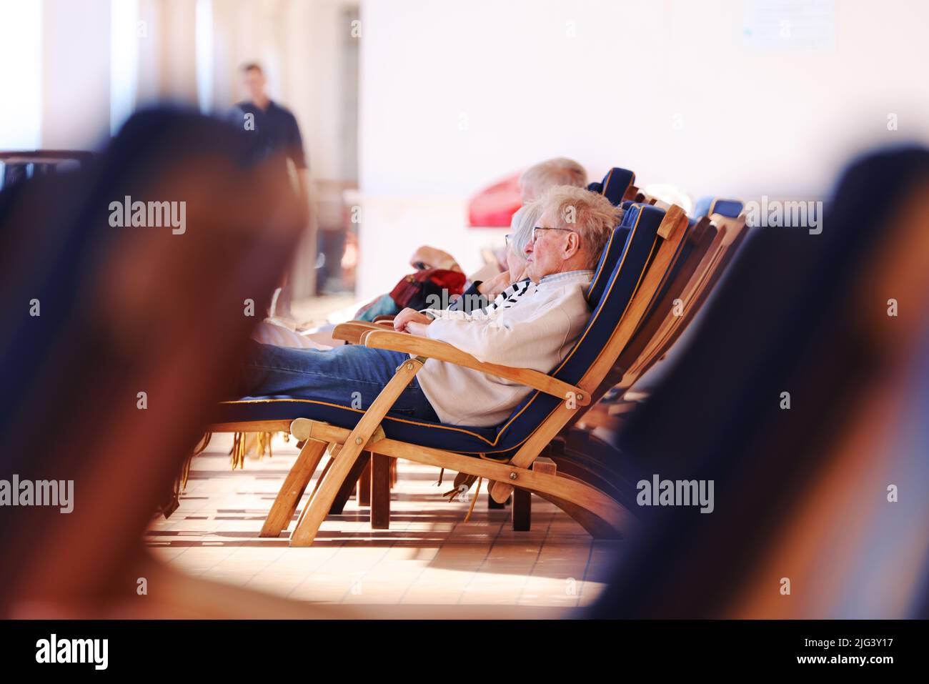 Ältere Passagiere entspannen sich auf einem sonnigen Kreuzfahrtdeck, während die Industrie nach der Coronavirus-Pandemie langsam wieder in den normalen Betrieb zurückkehrt. Stockfoto