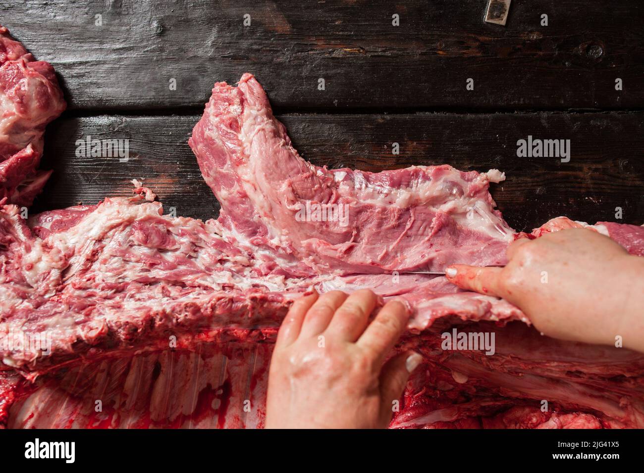 Metzger schneidet rohes Schweinekotelett. Holzhintergrund Stockfoto