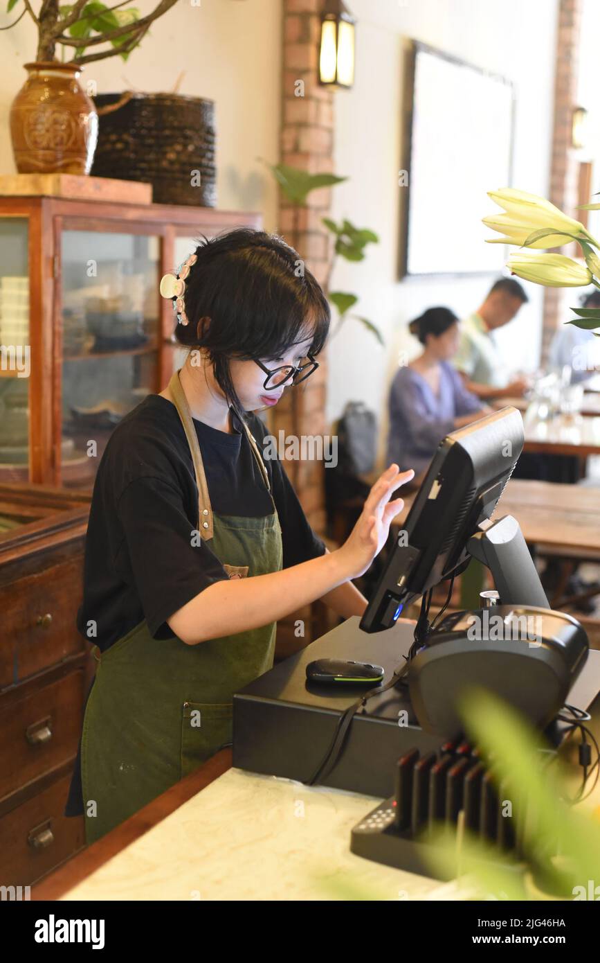 Junge vietnamesische Kellnerin serviert einen Kunden an der Kasse im Café. Stockfoto