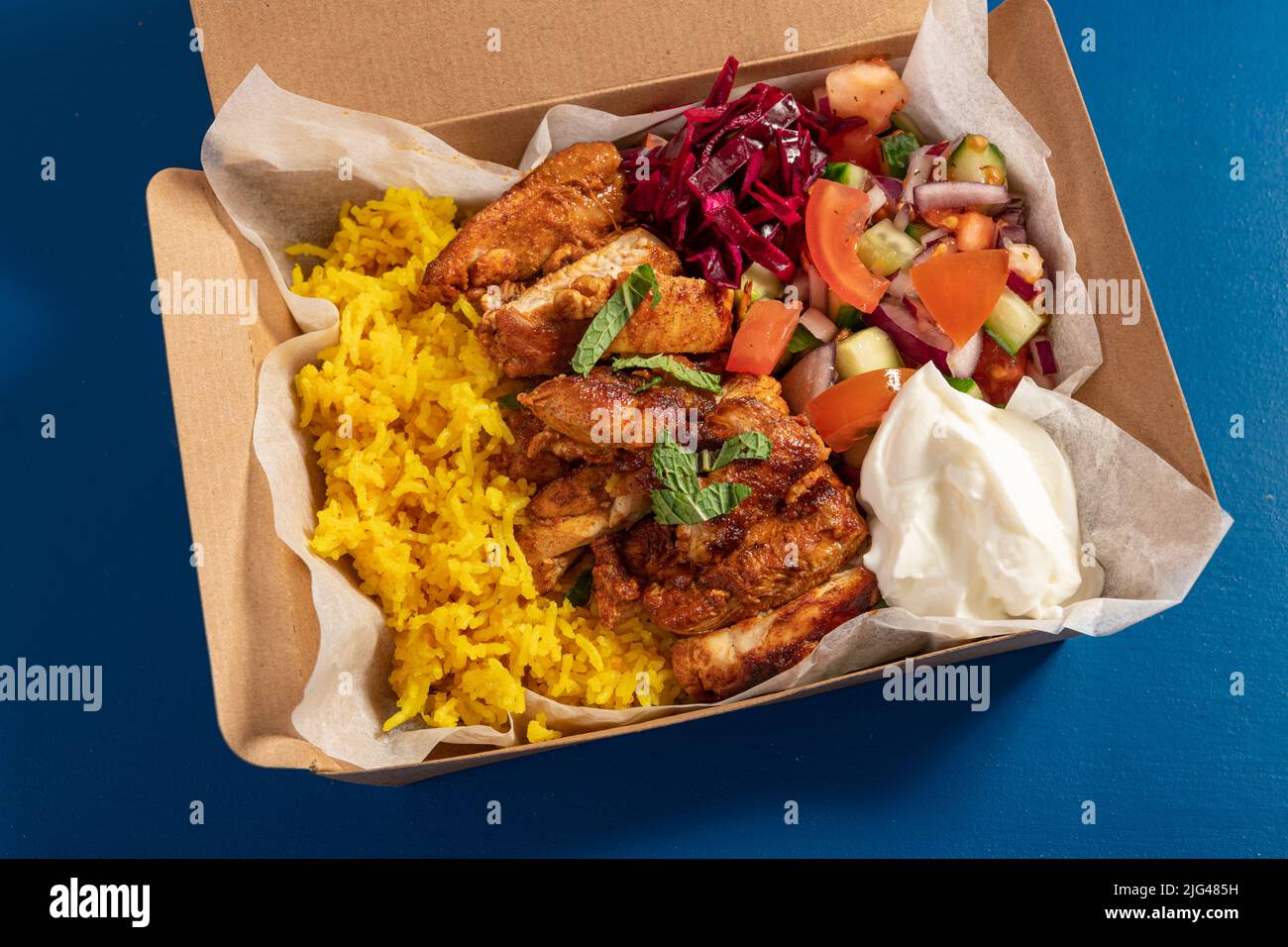 Traditionelles östliches mediterranes Essen zum Mitnehmen mit gegrilltem Hähnchen, gelbem Reis, frischem Salat und Joghurt in Kartonverpackung Stockfoto