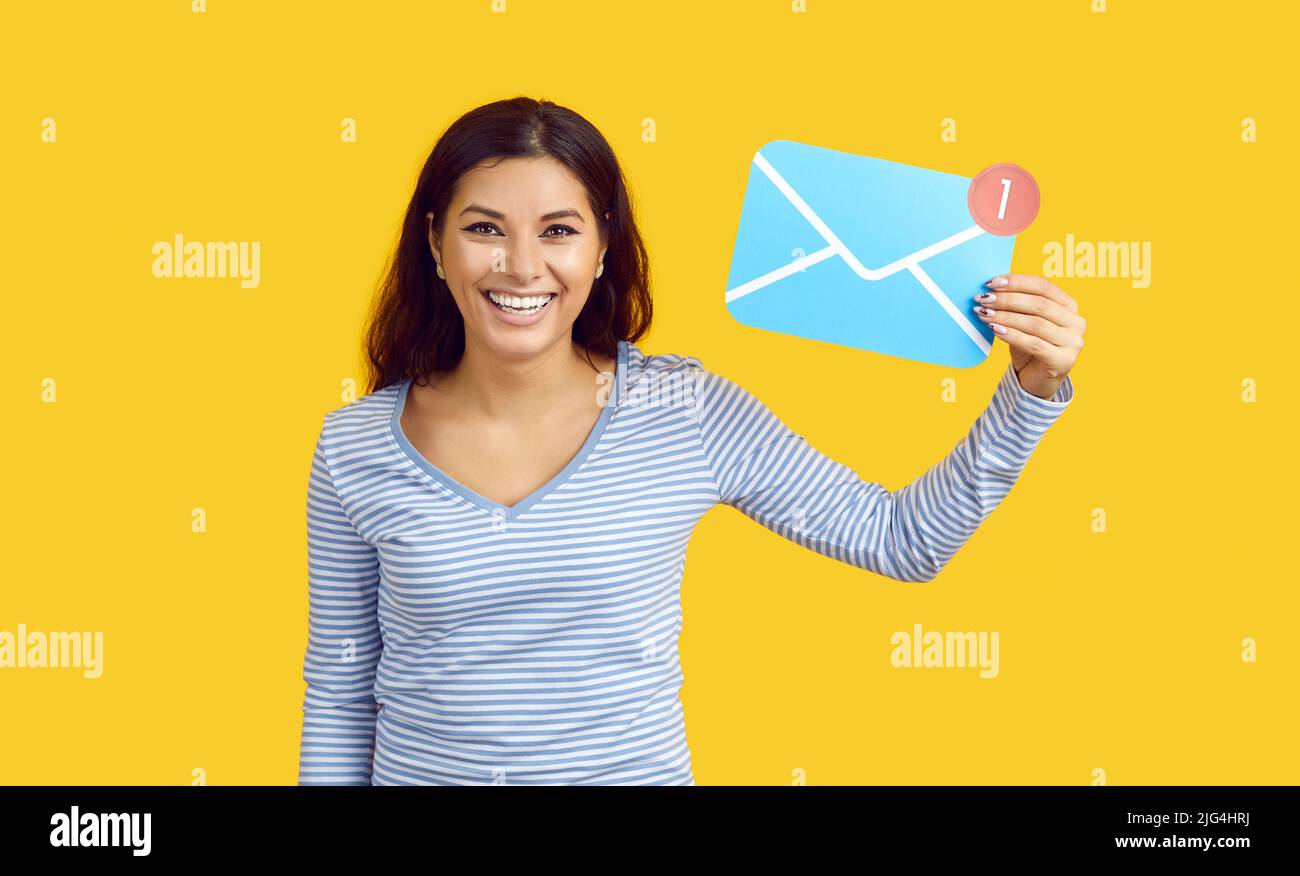 Fröhliche Frau mit einem E-Mail-Schild auf Papier und einer eingehenden Nachricht auf lebhaft gelbem Hintergrund. Stockfoto