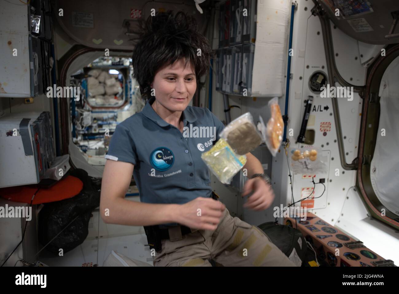Internationale Raumstation Expedition 67 die Flugingenieurin Samantha Cristoforetti der ESA posiert mit schwerelos fliegenden Nahrungsmittelpaketen im Modul Unity an Bord des umkreisenden spacelabs, 2. Juli 2022 in Earth Orbit. Stockfoto