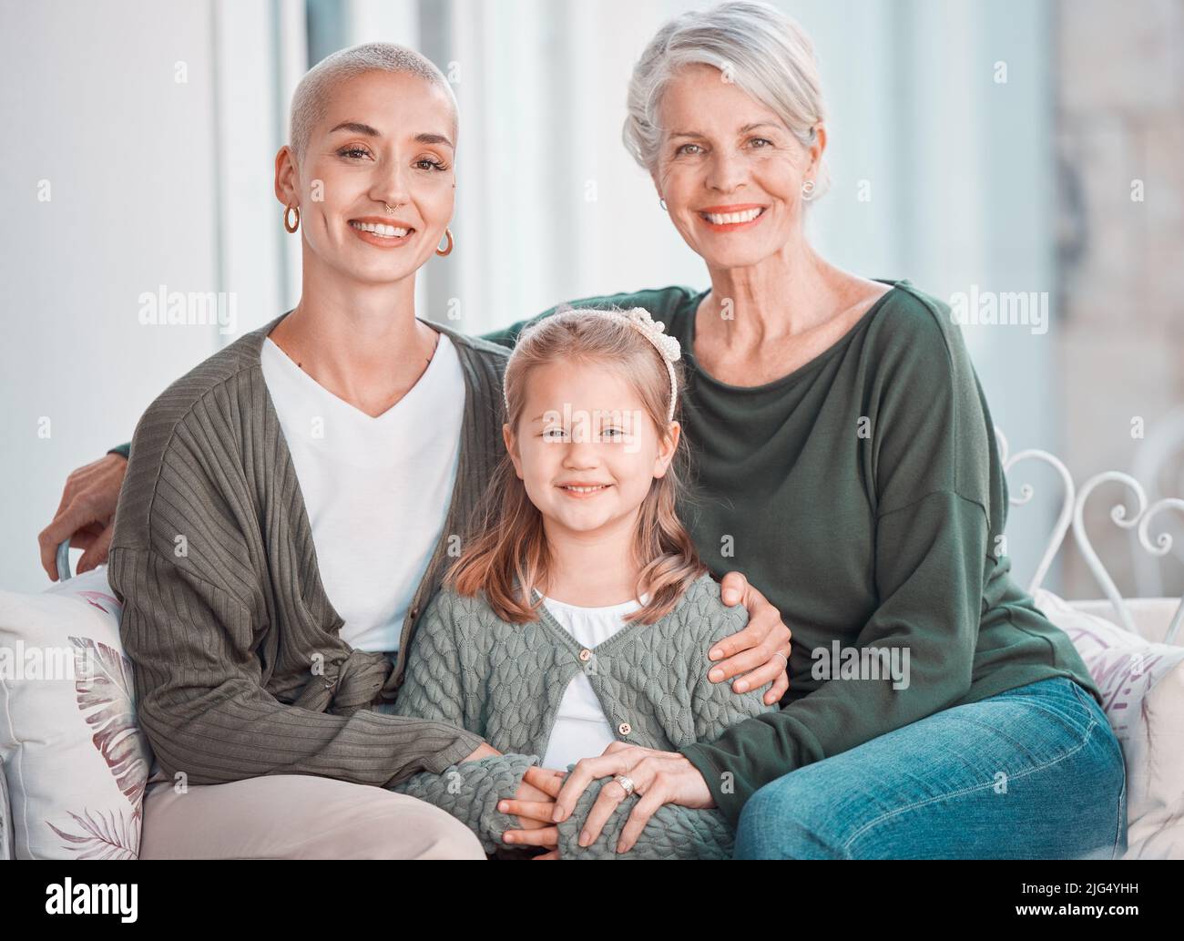 Drei Generationen von Frauen sitzen zusammen und schauen auf die Kamera. Porträt eines entzückenden kleinen Mädchens, das sich mit ihrer Mutter und Großmutter verklebt Stockfoto