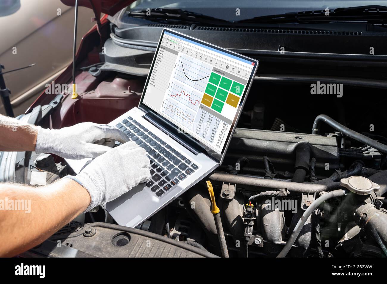 Junge männliche Mechaniker mit Laptop während der Prüfung Auto Motor Stockfoto