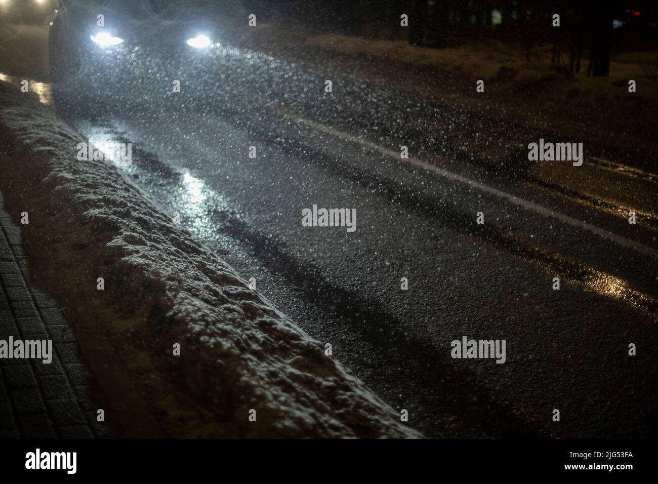 Auto in der Nacht im Schnee. Fahrzeuge auf der Straße mit eingeschalteten Scheinwerfern. Licht von den Lampen der Maschine. Stockfoto