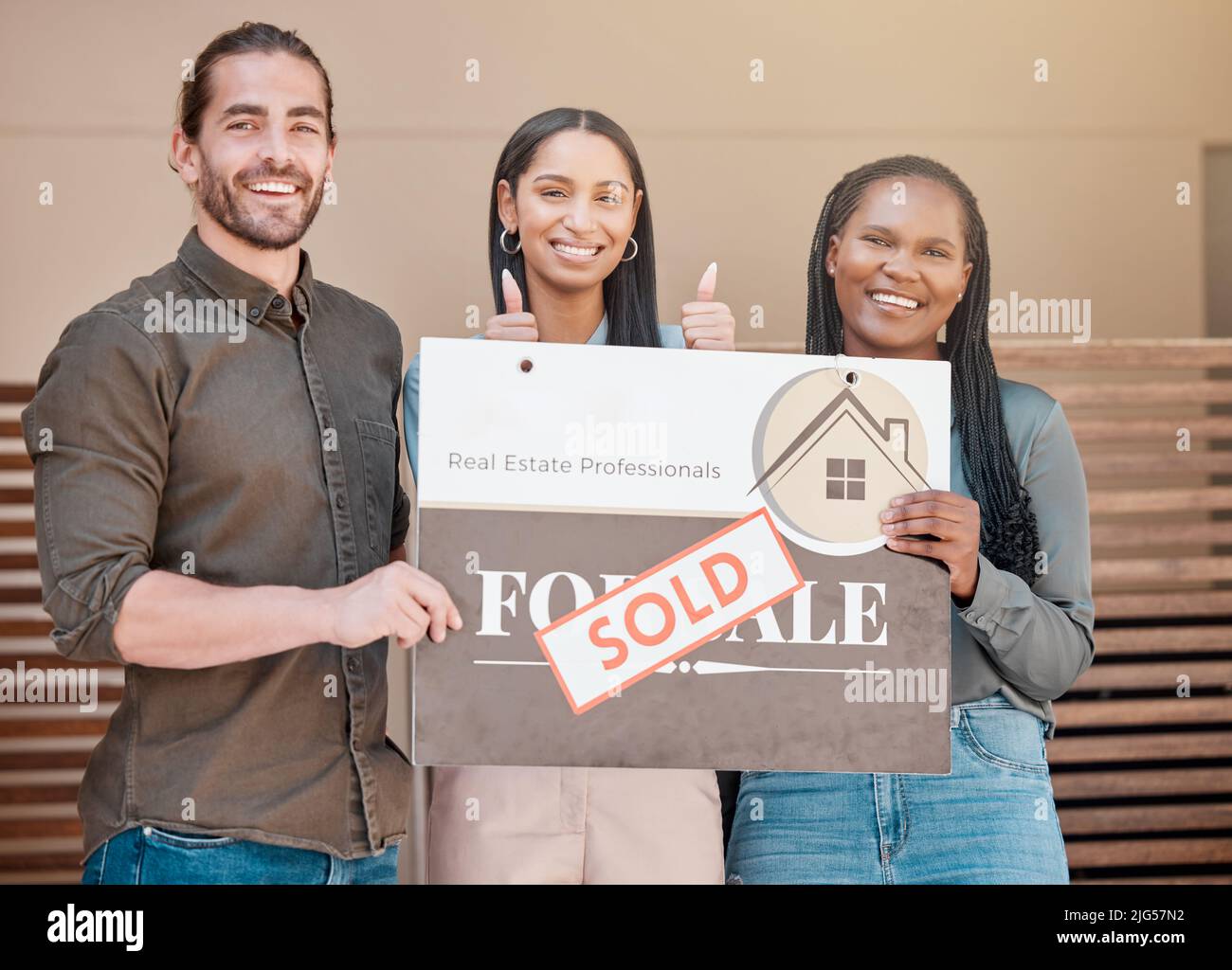 Erfolgreiche Hausbesitzer. Aufnahme eines jungen Paares und ihres Immobilienmaklers, die ein verkauftes Brett vor ihrem Haus halten. Stockfoto