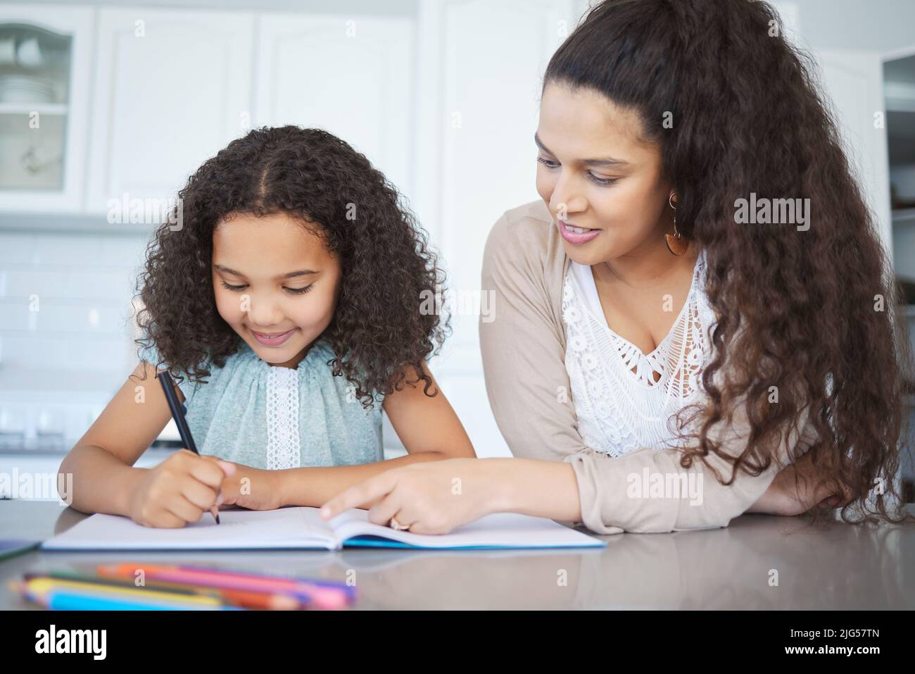 Sie liebt Heimschule. Aufnahme einer Mutter, die ihrer Tochter bei den Hausaufgaben am Küchentisch hilft. Stockfoto