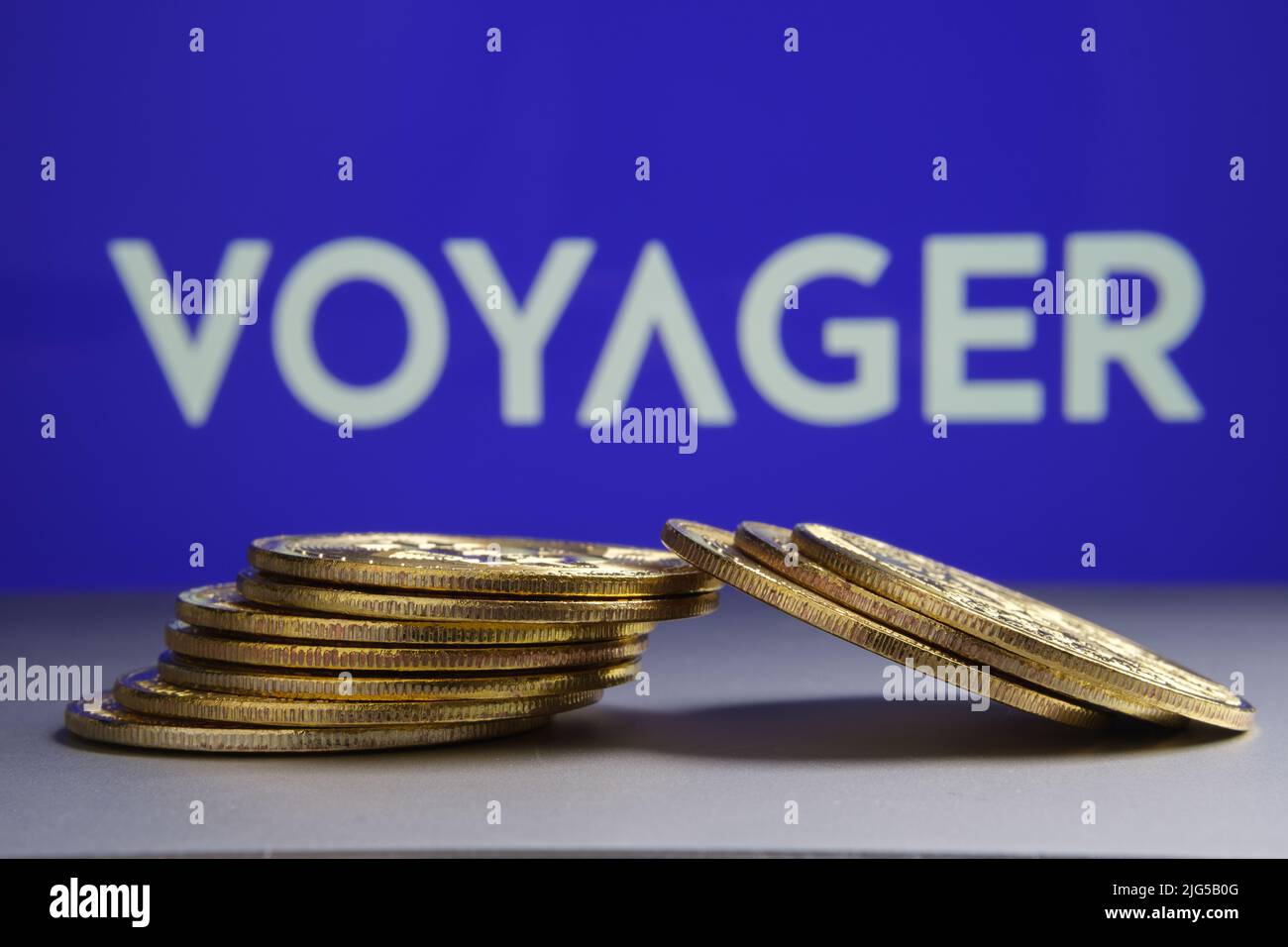 Gefallener Stapel Krypto-Münzen vor dem Bild und verschwommenes Firmenlogo der Voyager Digital Ltd auf verschwommenem Hintergrund. Konzept für Insolvenz. Stafford, United Kin Stockfoto