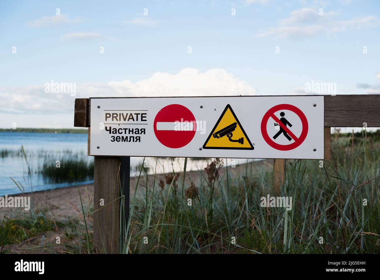 Ein 'Private Property'-Schild an einem Strand in Europa. Konzentrieren Sie sich auf Zeichen mit Logos. Entkochte Sandküste und Meer dahinter. Kein Zutritt, keine Umleitung Stockfoto