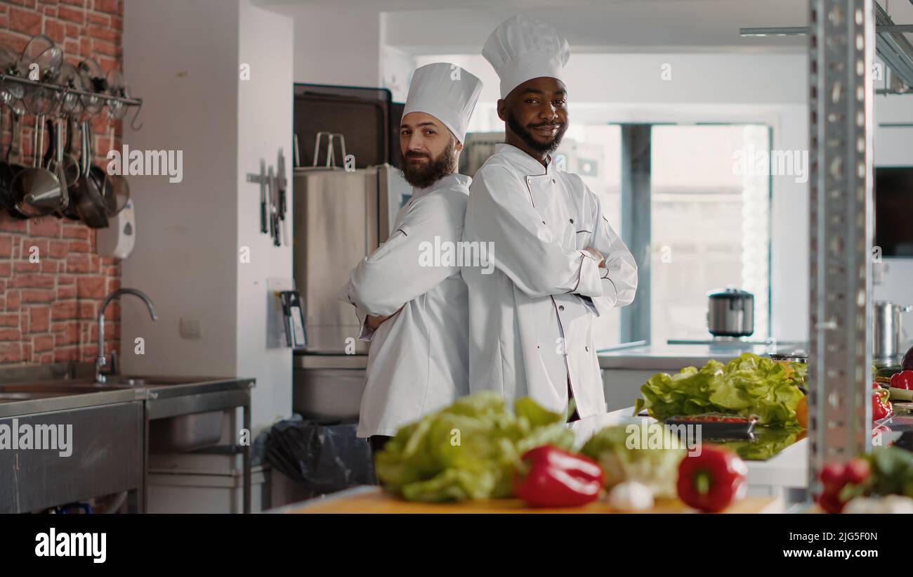 Porträt eines vielfältigen Teams, das in der professionellen Restaurantküche posiert und sich bereit macht, Gourmet-Gerichte zu kochen. Köche in Uniform machen Gericht Zubereitungen mit Lebensmittelzutaten für Gastronomie Rezept. Stockfoto
