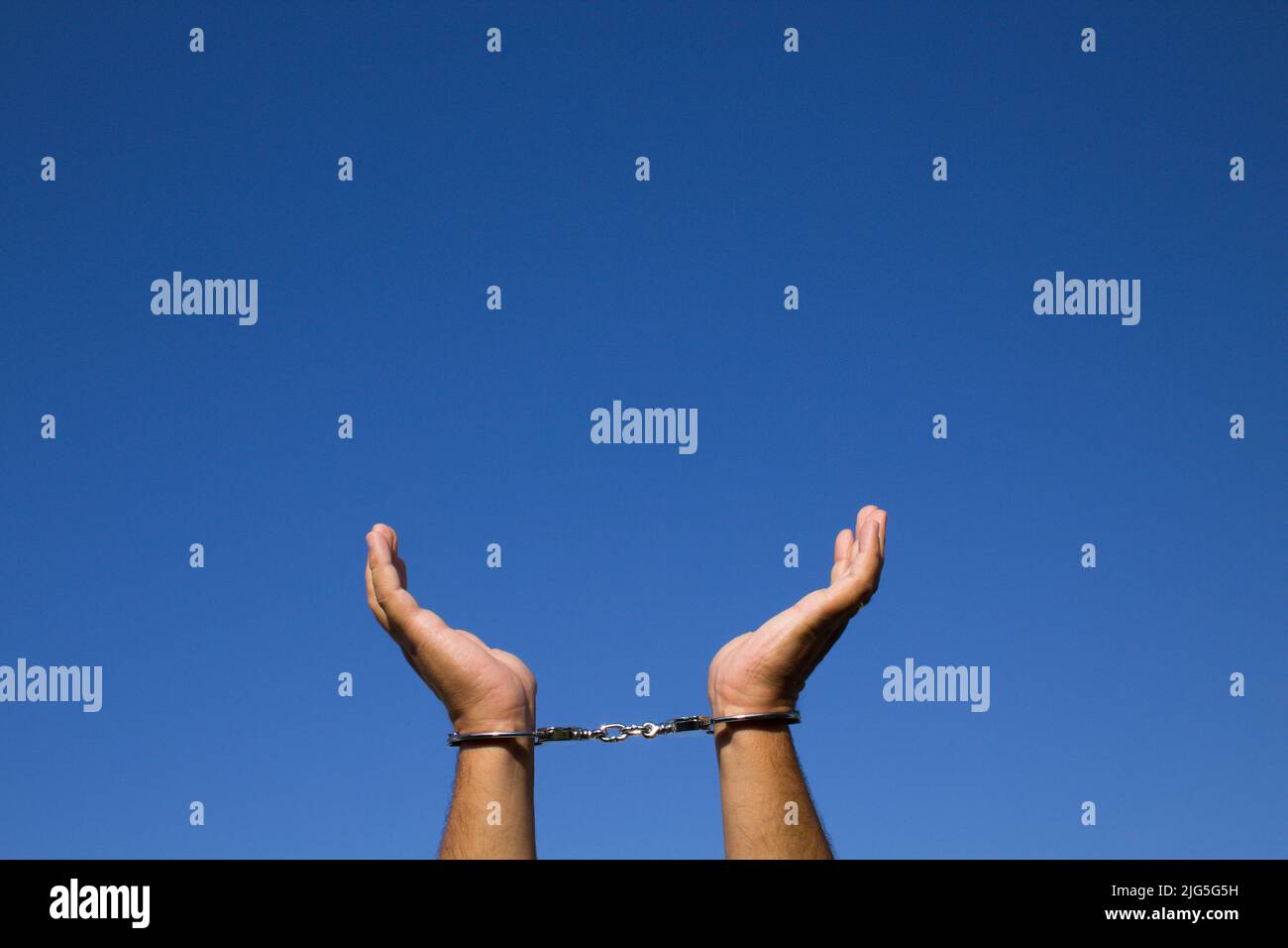 Bild der Hände eines Mannes, der nach der Verhaftung mit Handschellen an seinen Handgelenken in den Himmel blickt. Bezug auf Freiheit Stockfoto