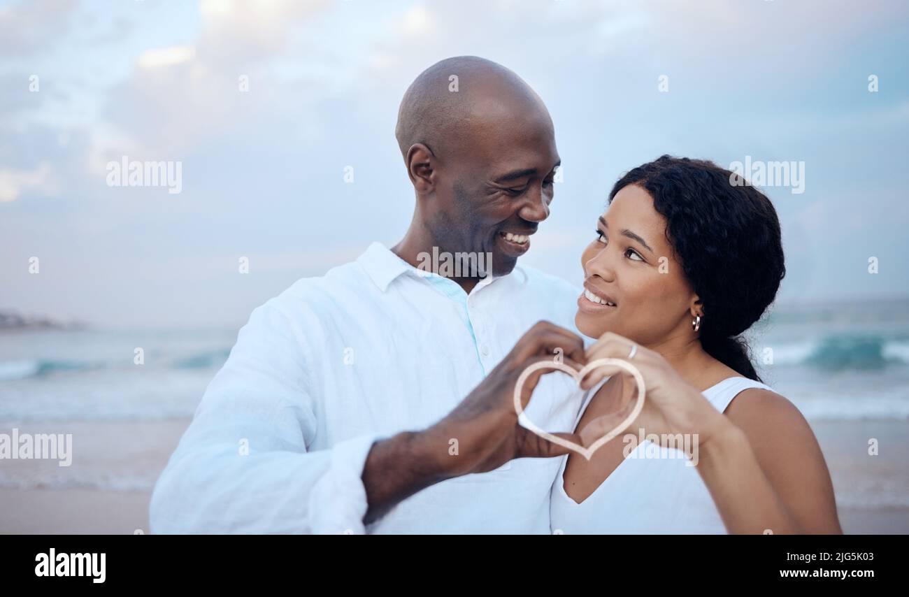 Ein Mann machte ganz. Aufnahme eines schönen Paares, das mit den Händen ein Herz macht, während es sich am Strand festhält. Stockfoto
