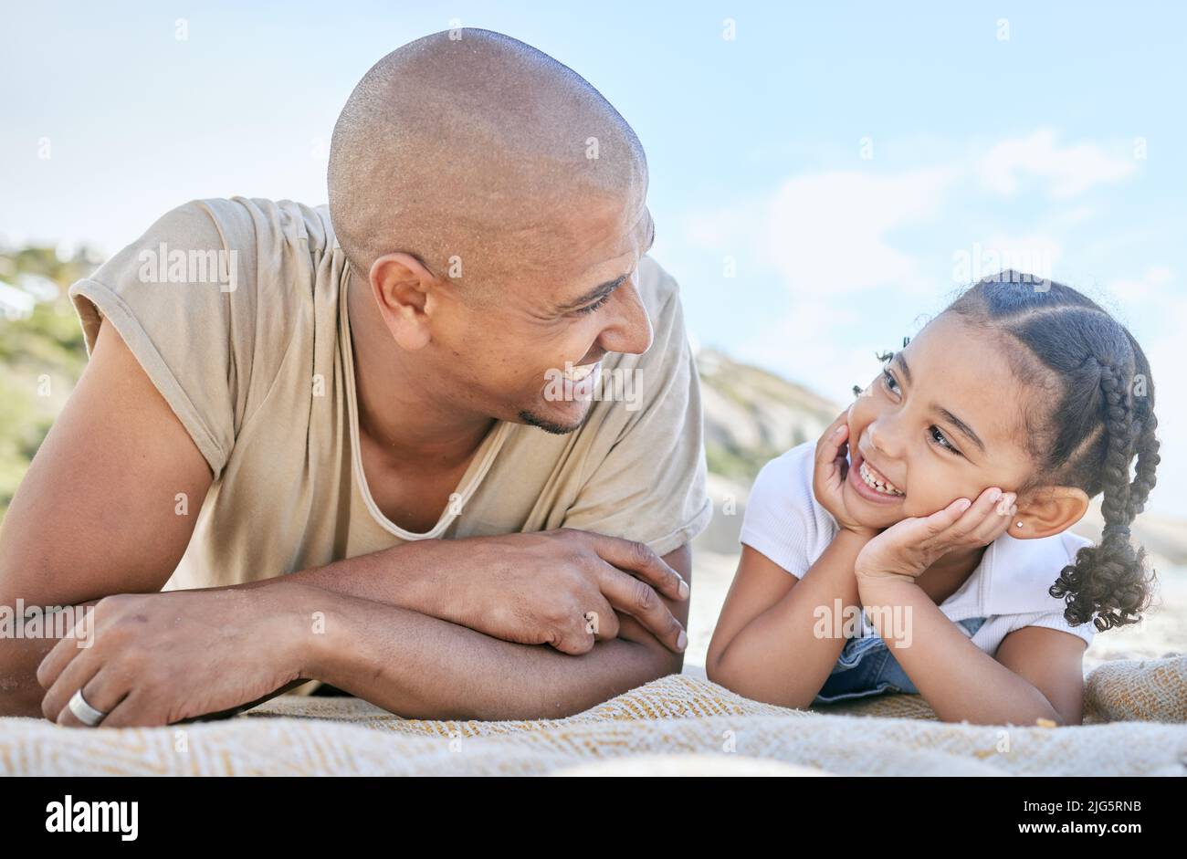 Lächelnder, alleinerziehender Vater und kleine Tochter, die sich beim Entspannen am Strand gegenseitig anschauten. Liebenswert Mädchen Bonding mit ihrem Vater und genießen Urlaub Stockfoto