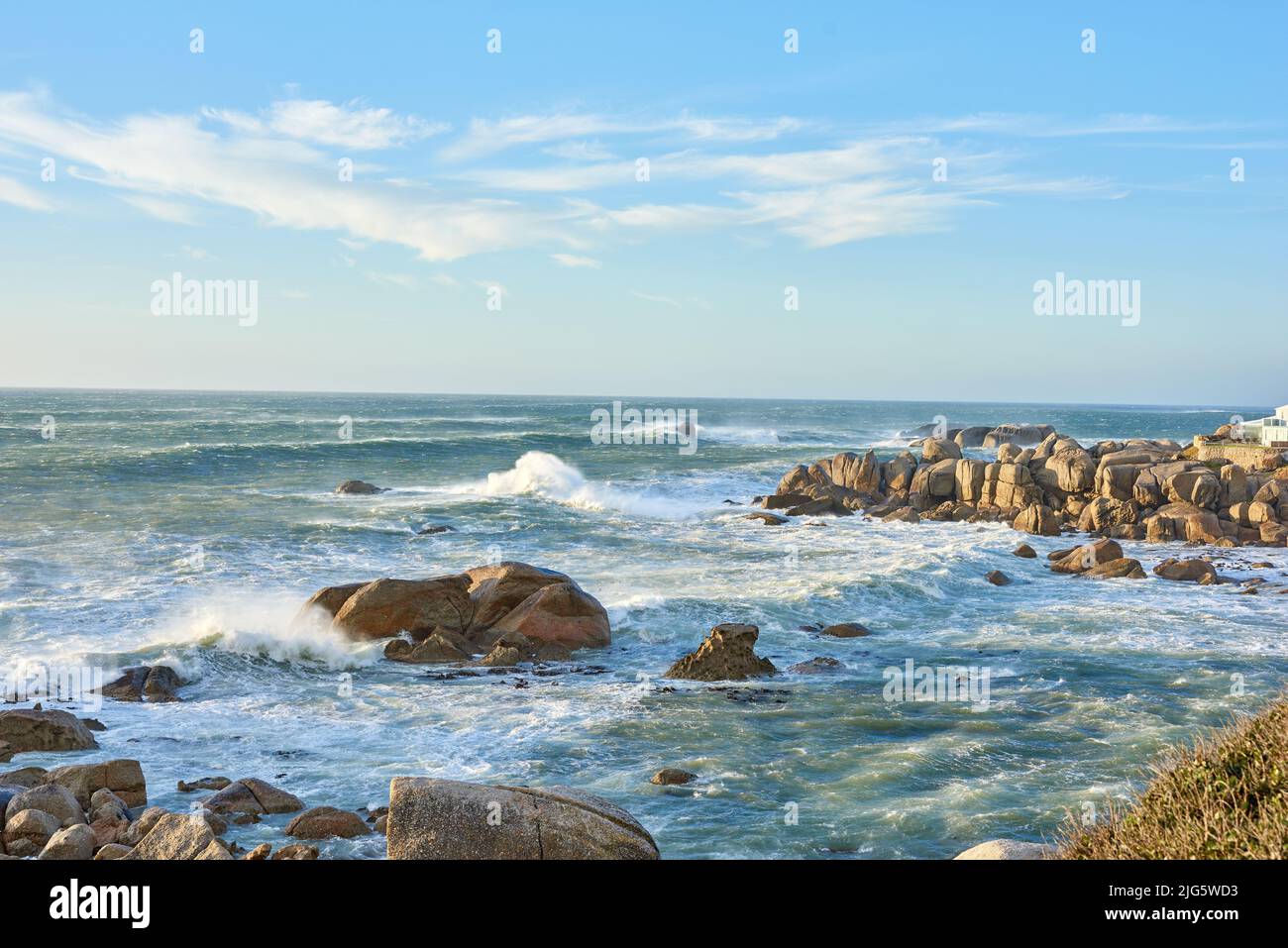 Copyspace auf dem Meer mit einem wolkigen blauen Himmel Hintergrund und felsigen Küste in Western Cape Südafrika. Meereswellen krachen an einem Strand auf Felsbrocken Stockfoto
