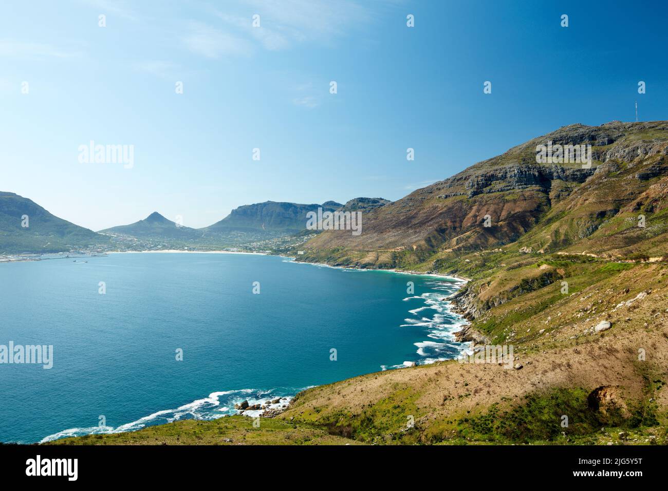 Landschaft mit felsiger Küste in der Nähe von Bergen in Südafrika für eine friedliche Naturszene. Großer blauer See oder ruhiges Meer, umgeben von lebhaften grünen Hügeln Stockfoto