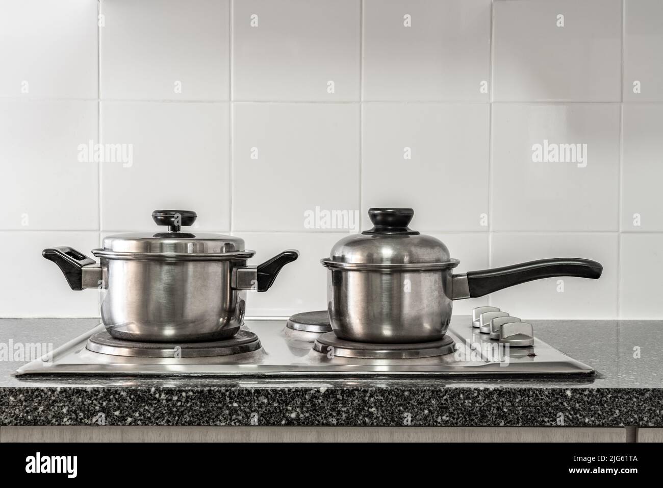 Ein paar rostfreie Töpfe auf dem Küchenherd mit Marmorplatte und weißer Fliesenwand Stockfoto