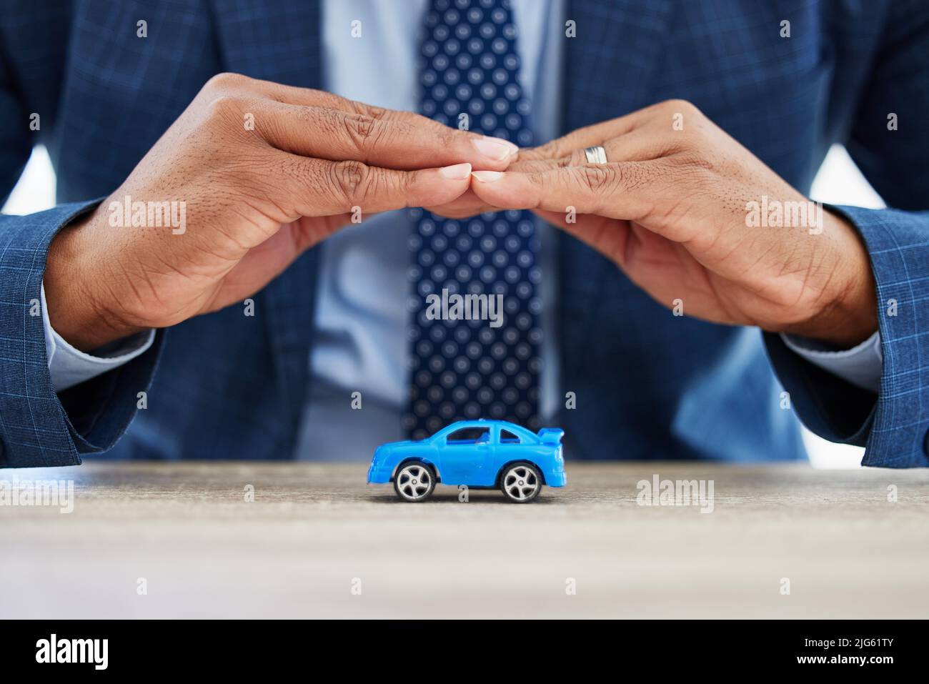 Reparatur das Dach ist, wenn die Sonne scheint. Aufnahme eines nicht erkennbaren Geschäftsmannes, der zu Hause ein Spielzeugauto mit seinen Händen bedeckt. Stockfoto