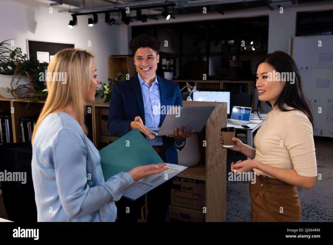 Lachende Kollegen aus verschiedenen Rassen, die spät in der Nacht über das Projekt im Büro sprechen, beim Brainstorming Stockfoto