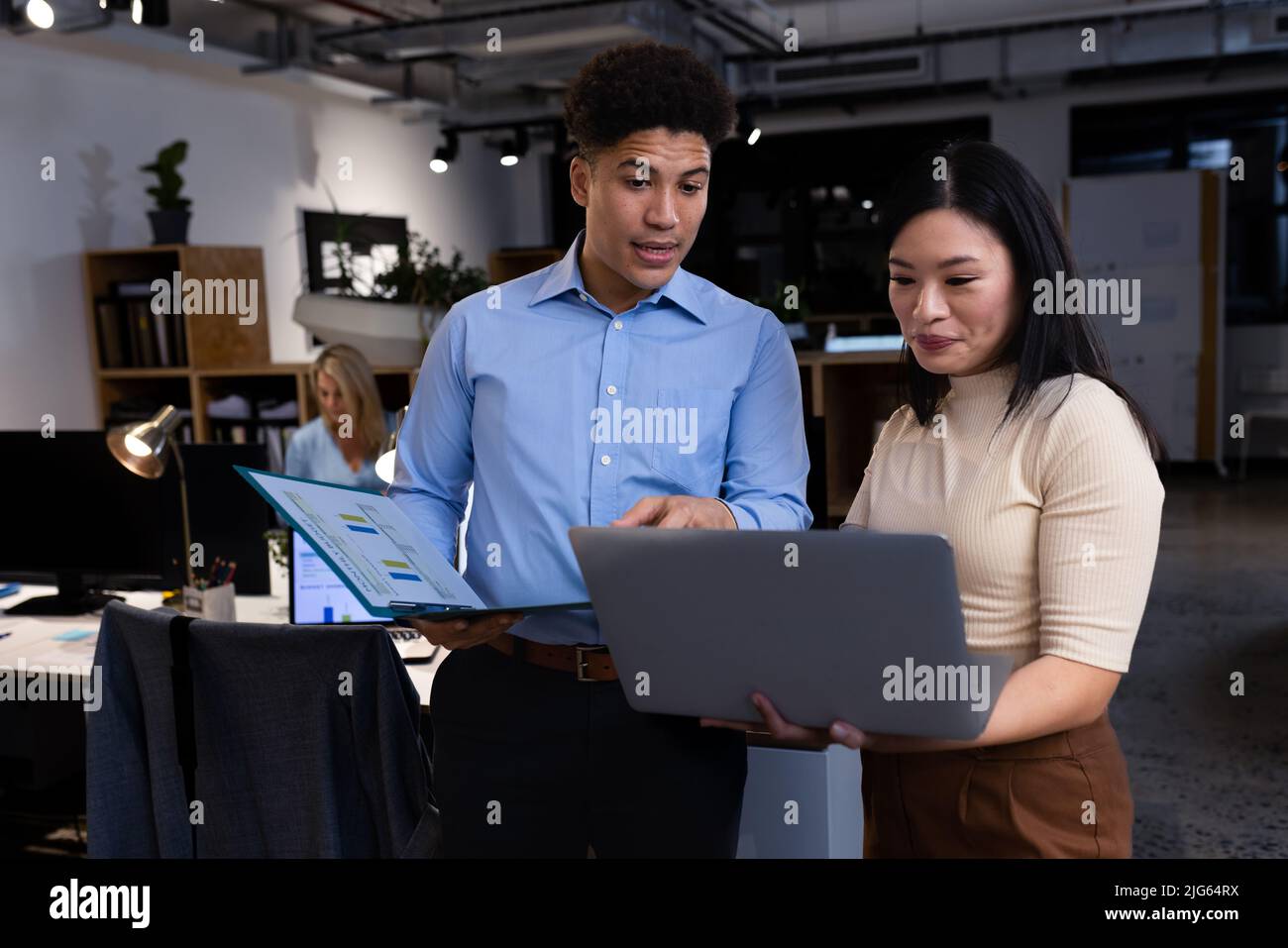 Asiatische Kollegen und Kolleginnen diskutieren über einen Laptop, während sie spät abends im modernen Büro arbeiten Stockfoto