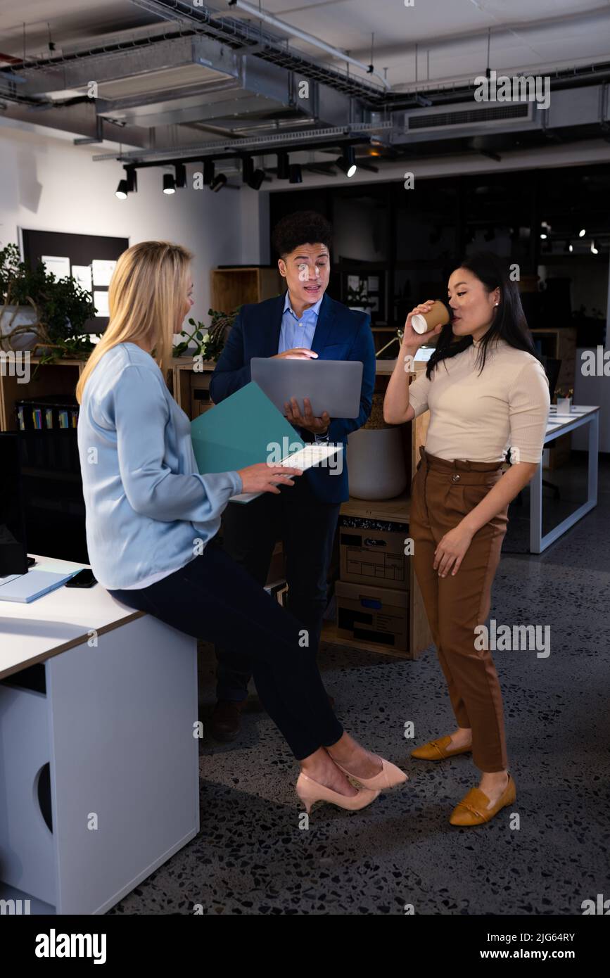 Multirassischer Geschäftsmann mit Laptop-Briefing weiblicher Kollegen, während er spät in einem modernen Büro arbeitete Stockfoto